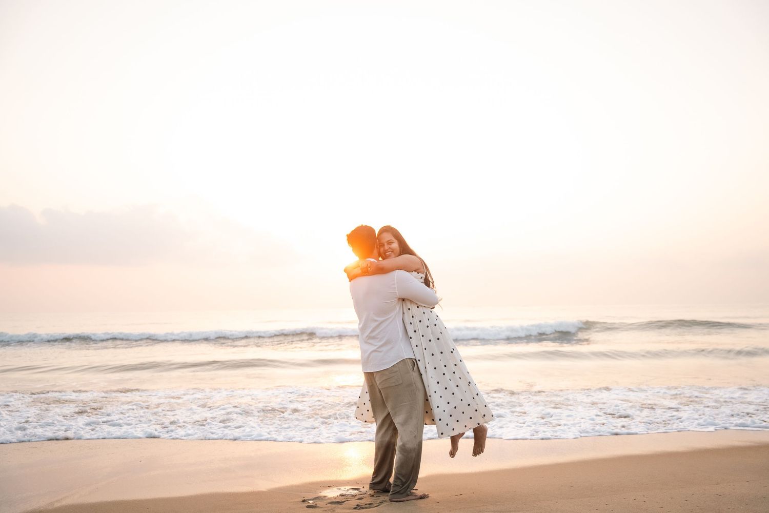 Couple embraces on beach at sunset with waves rolling in.