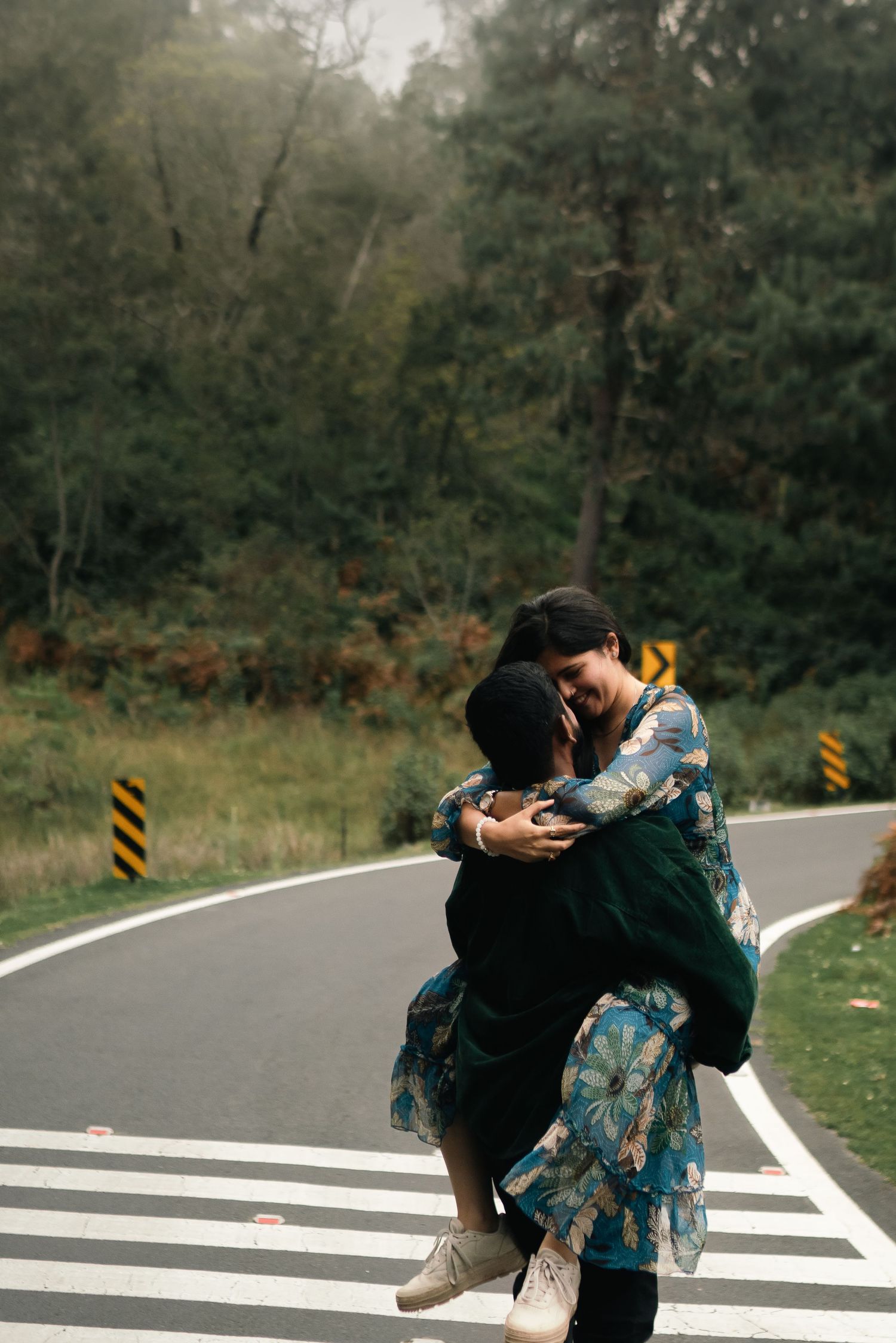 A romantic embrace on a curved forest road with a floral dress and black outfit.