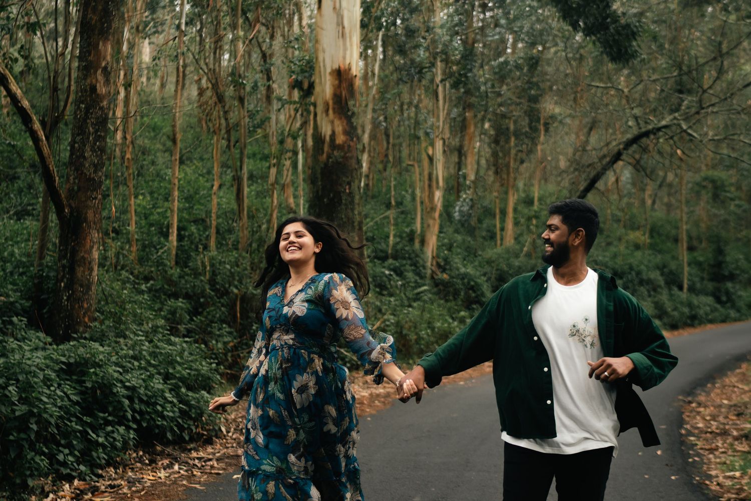 Happy couple walking hand in hand through a eucalyptus forest path.
