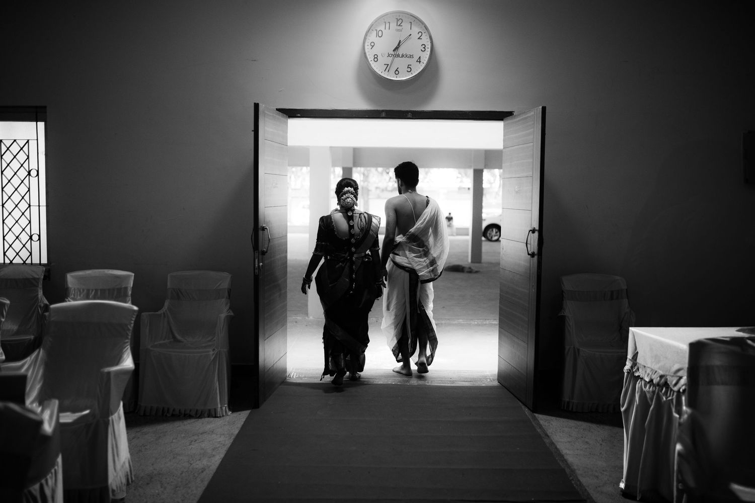 Silhouetted figures walk through minimalist hallways in dramatic black and white composition.