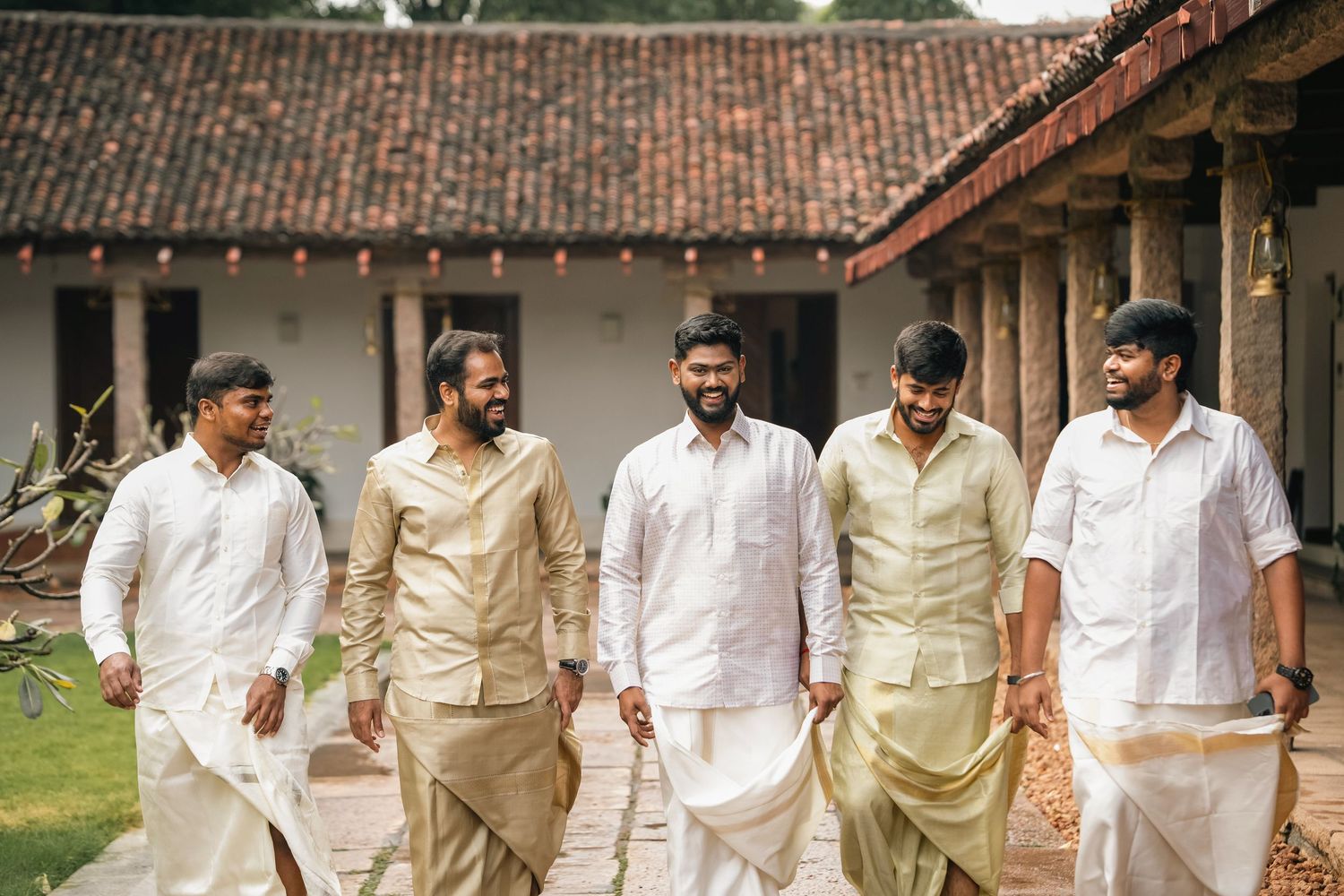 People walk in a line through a traditional courtyard wearing white and beige formal attire.