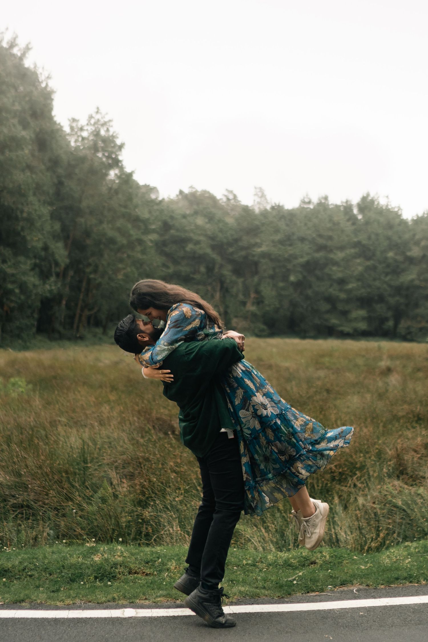 A couple sharing a joyful spinning embrace on a country road surrounded by green forest.