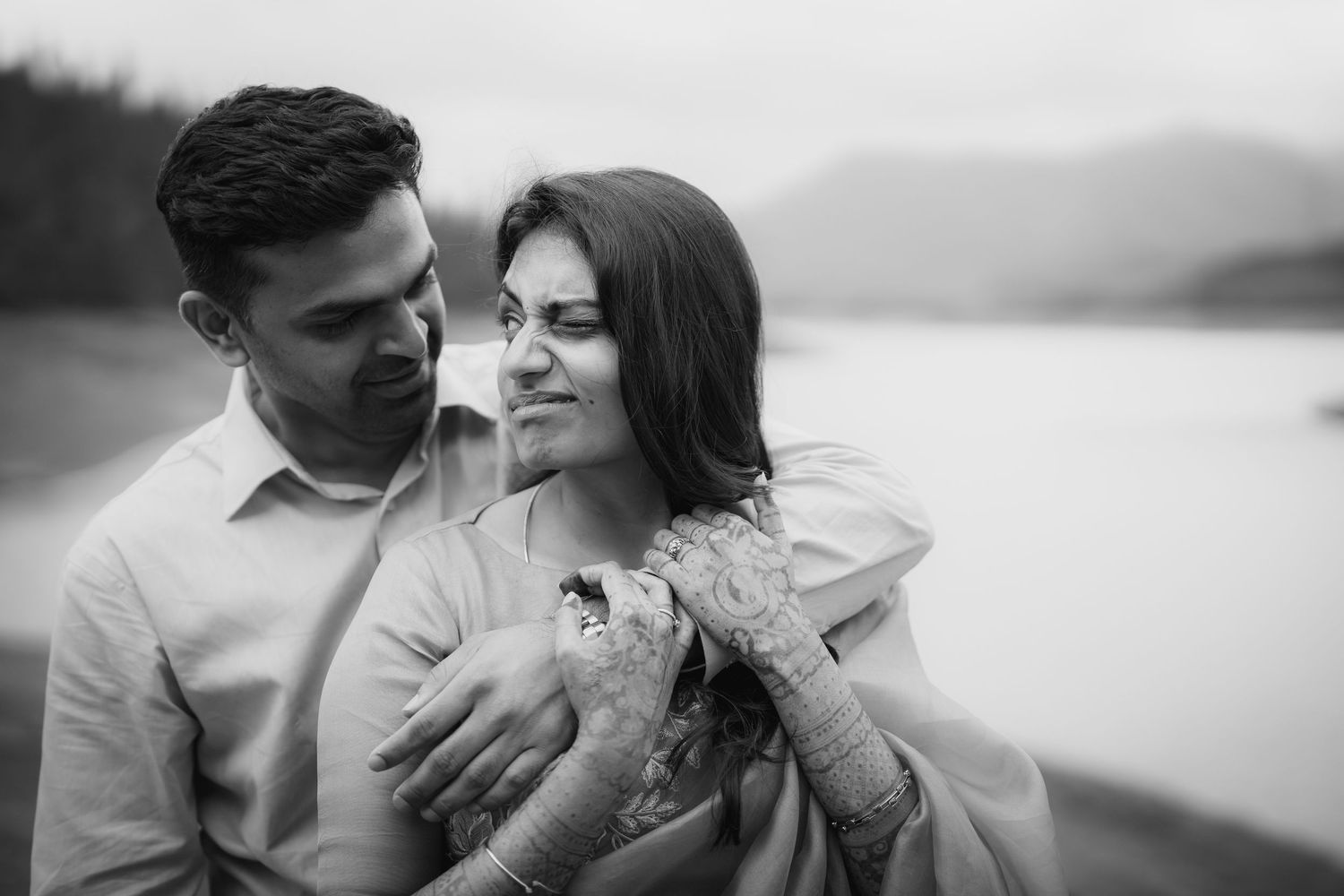Couple embracing in romantic photoshoot with scenic lake backdrop.