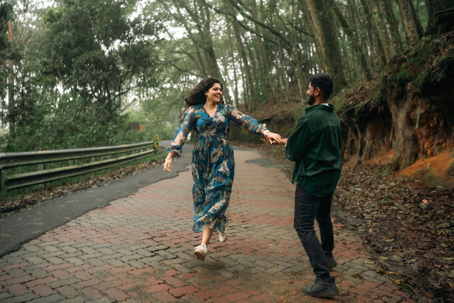 Playful couple dancing and holding hands on a forest trail.