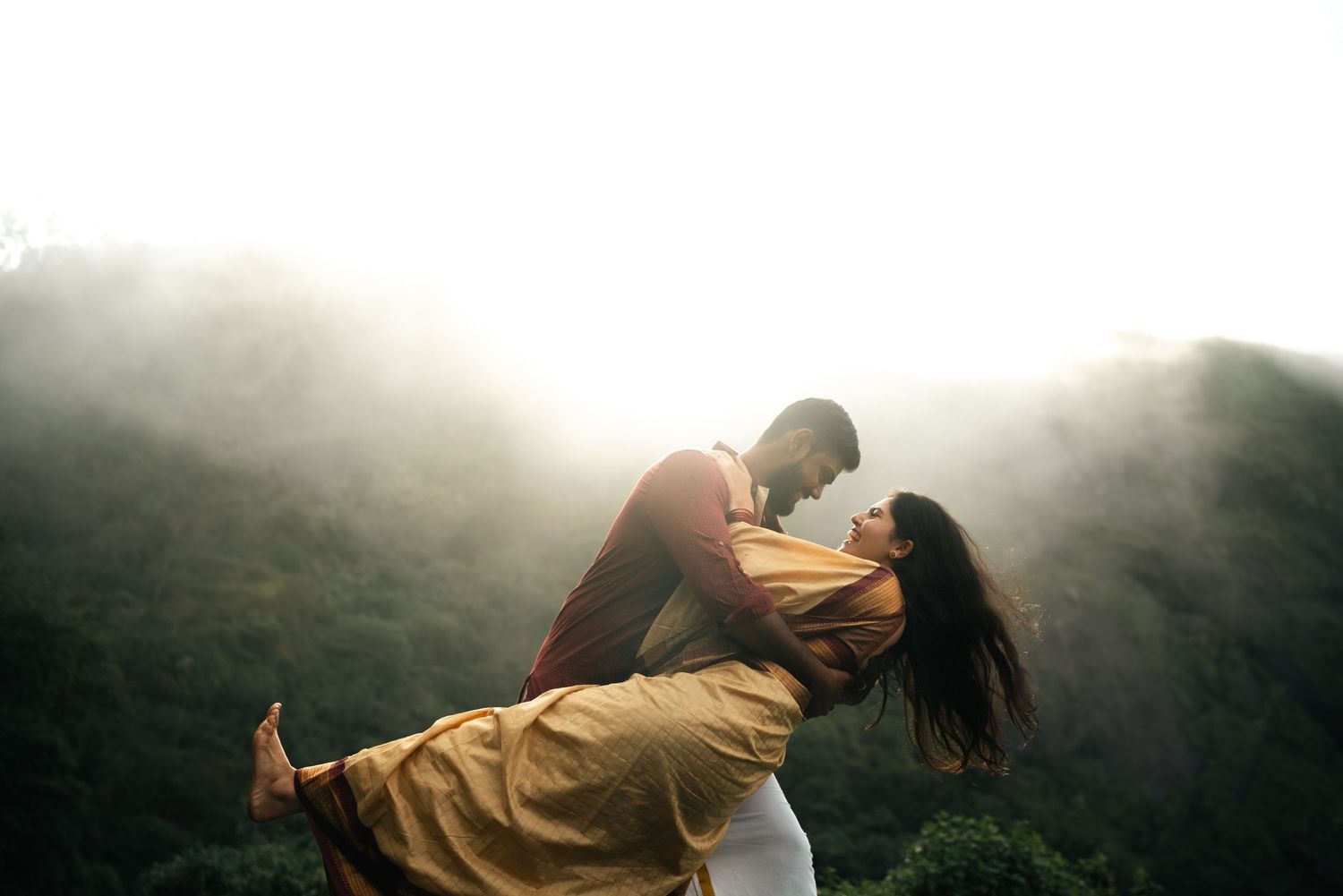A romantic lift pose captured against misty mountains in dramatic lighting.