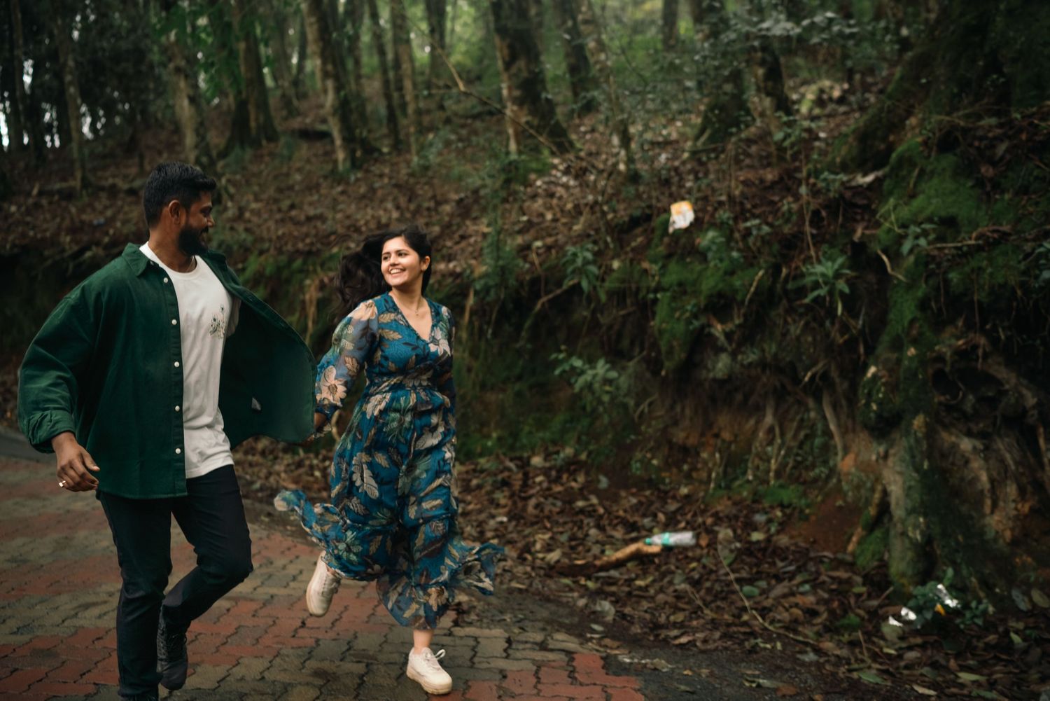Couple walking through a forest path surrounded by lush greenery.