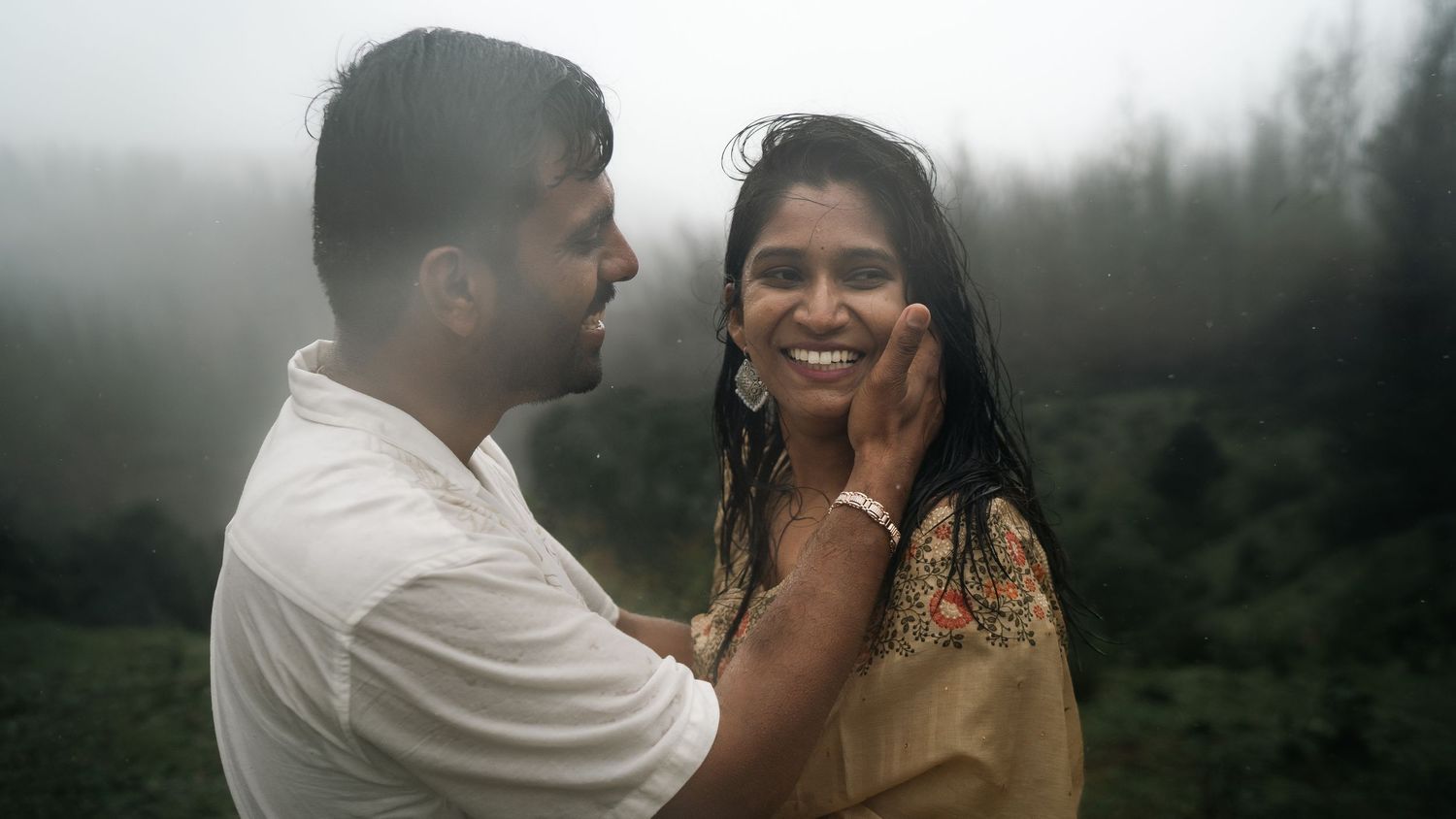 A romantic photoshoot near a misty lake with mountains in the background.