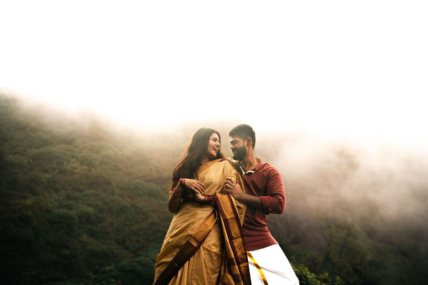Romantic couple embracing in a misty mountain setting at golden hour.