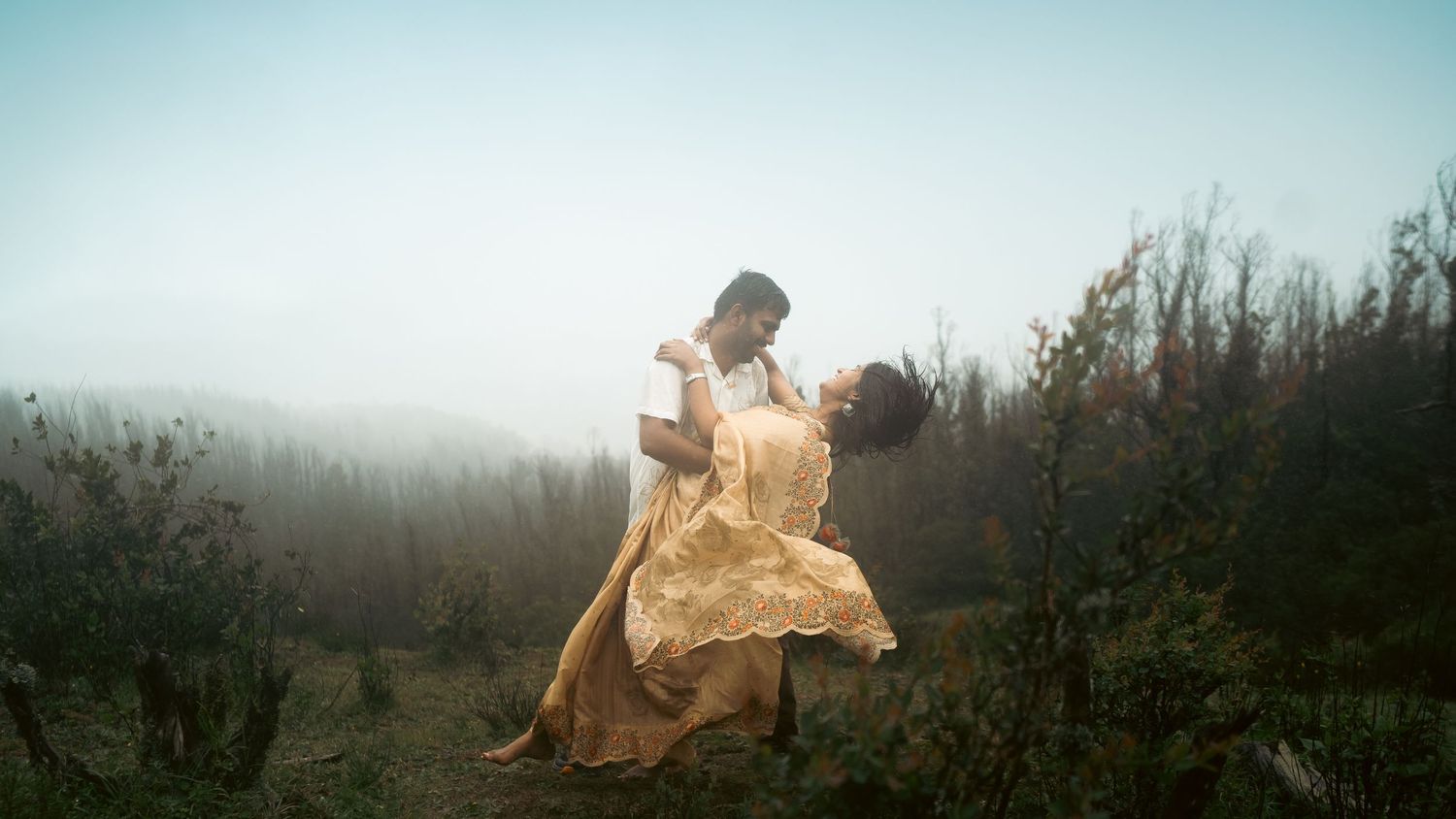 Wide panoramic shot of a couple posing against a misty mountain backdrop.