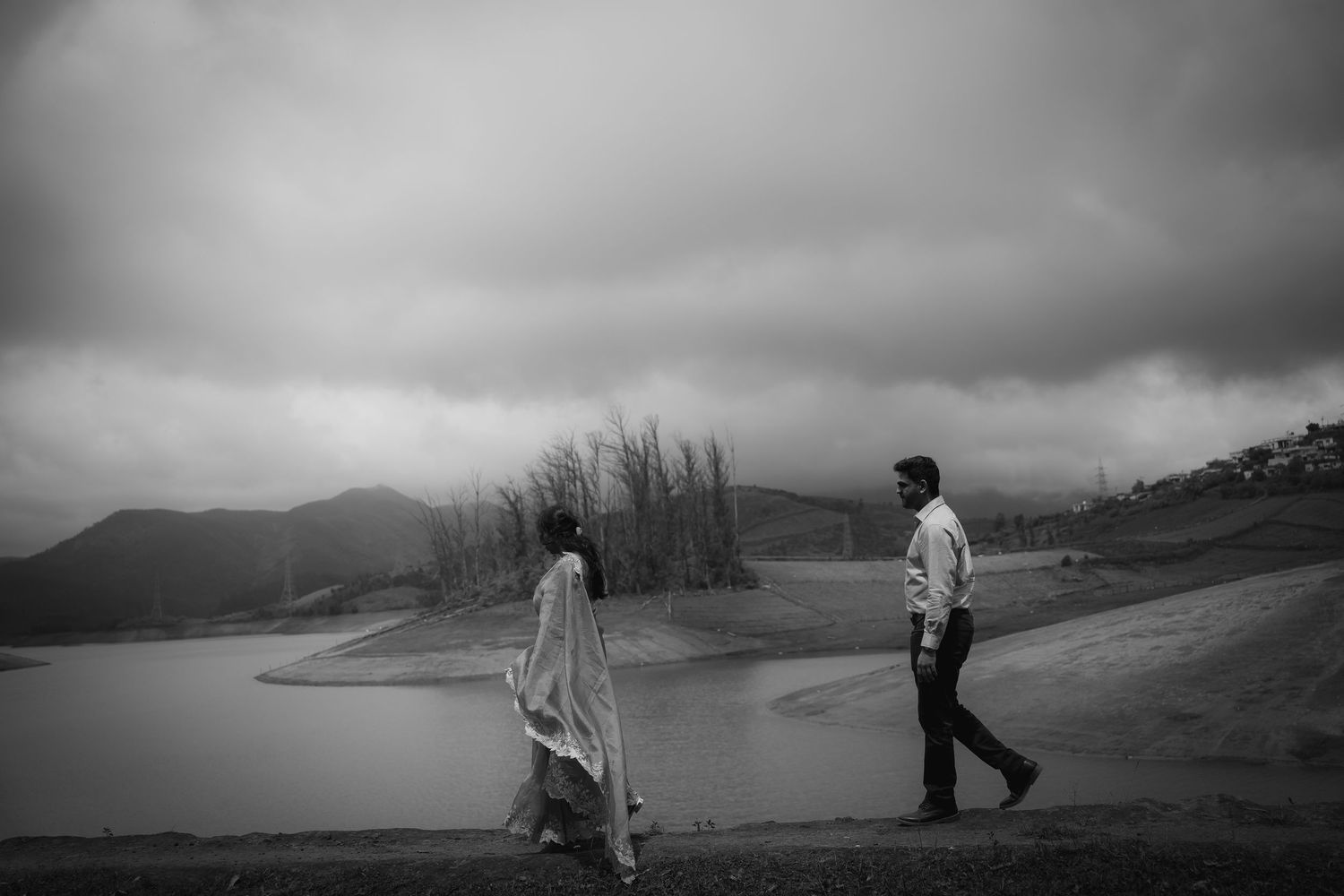 Moody black and white landscape photo with silhouettes against a lake backdrop.