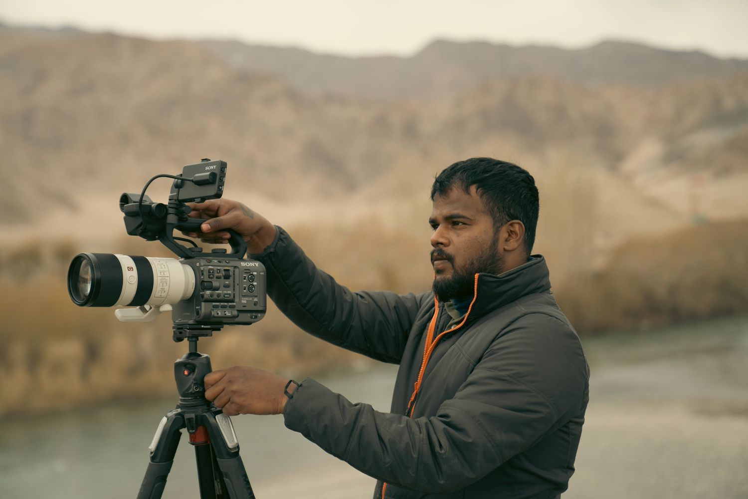 Professional photographer in a dark jacket takes outdoor photos with a telephoto lens in a desert landscape setting.