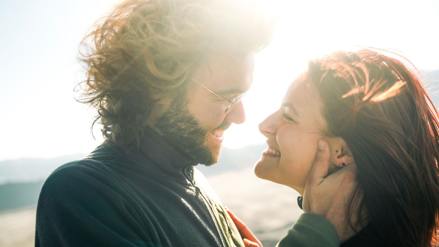 A silhouetted couple shares a romantic moment at sunset with sun rays streaming through their profiles.
