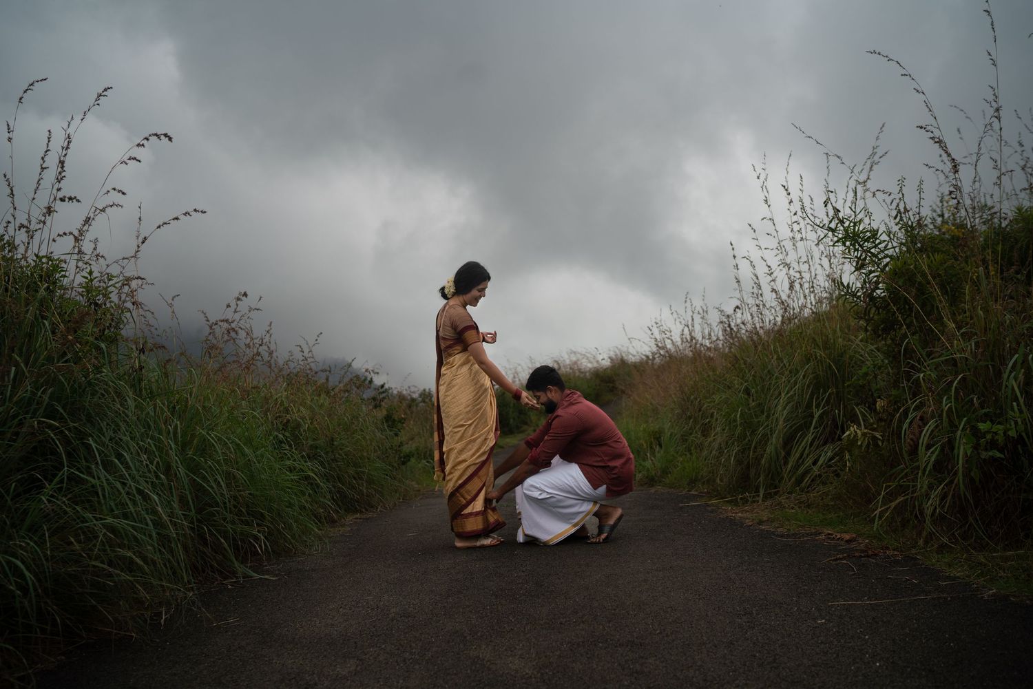 A tender moment captured on a misty path surrounded by wild grass and dark clouds.