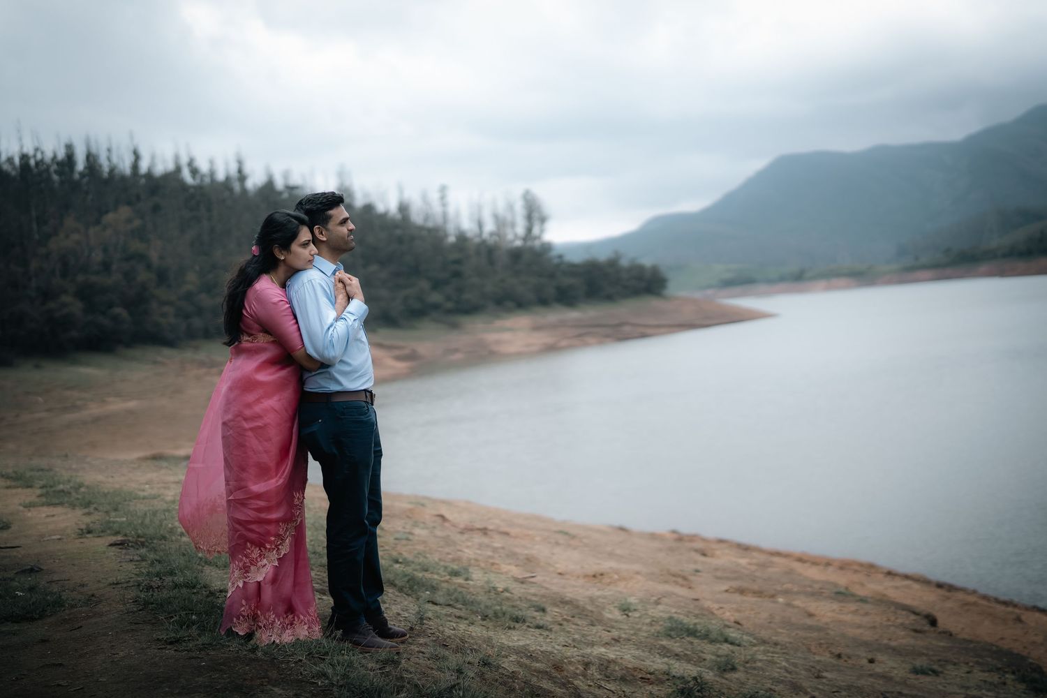 Couple sitting by scenic mountain lake with cloudy sky backdrop.