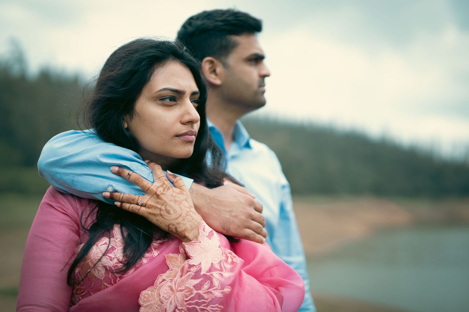 Romantic couple embracing by a scenic lake with mountains in the background.