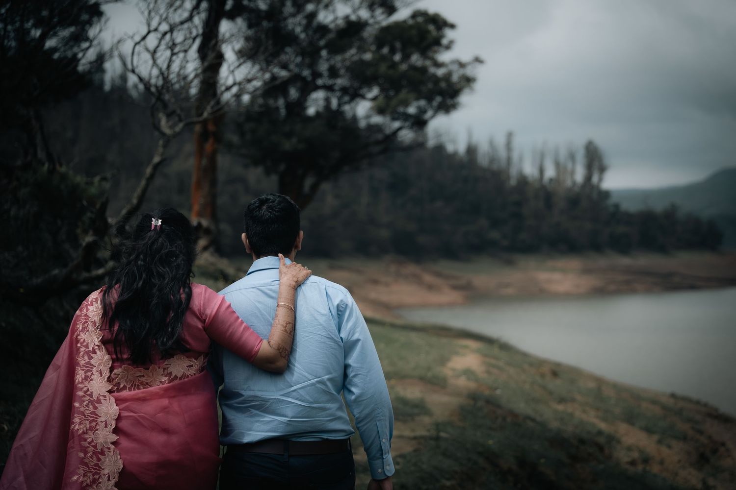 Romantic couple near lake with mountains and moody sky in background.