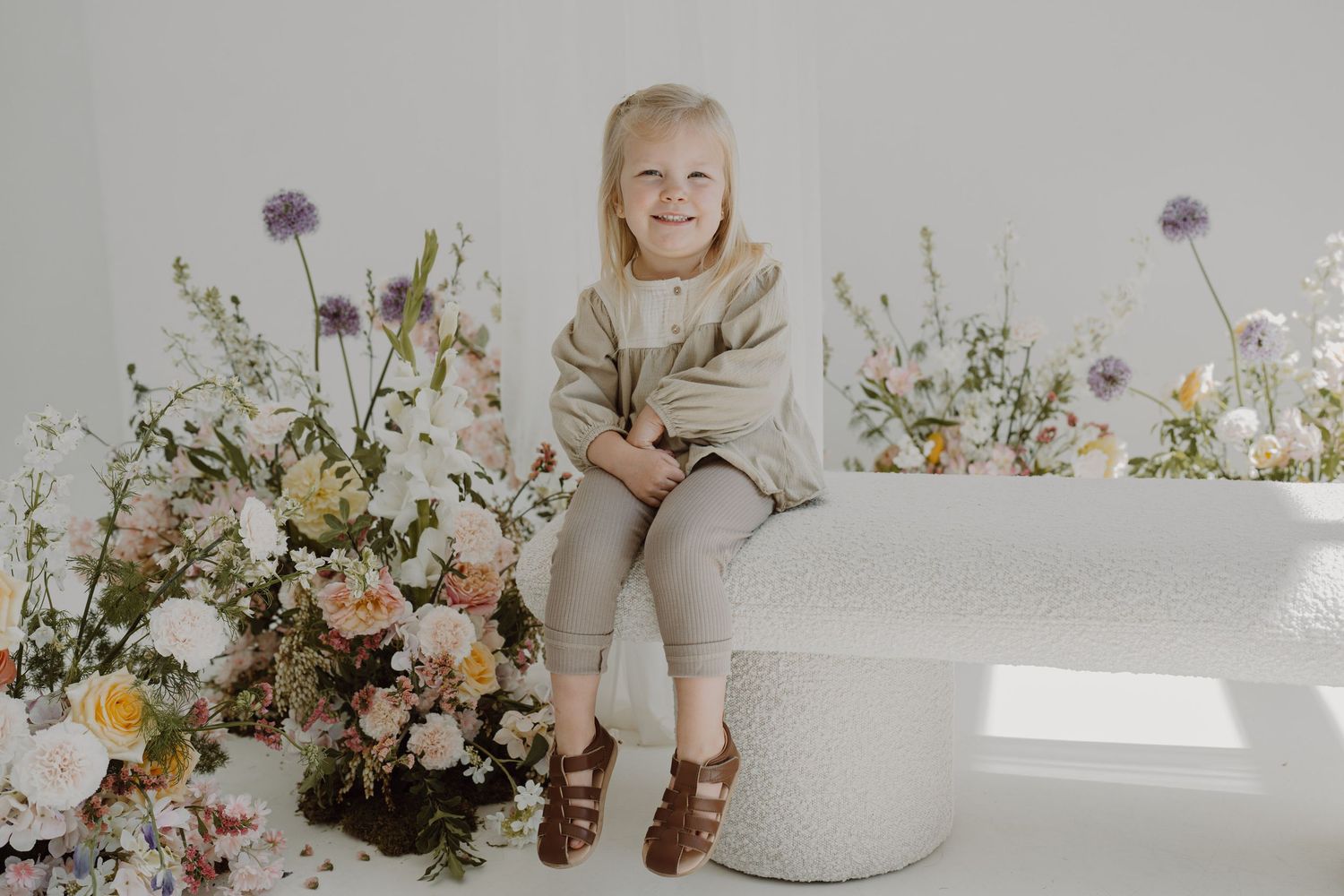 Portrait in a light-filled studio with wildflowers and a white circular ottoman.