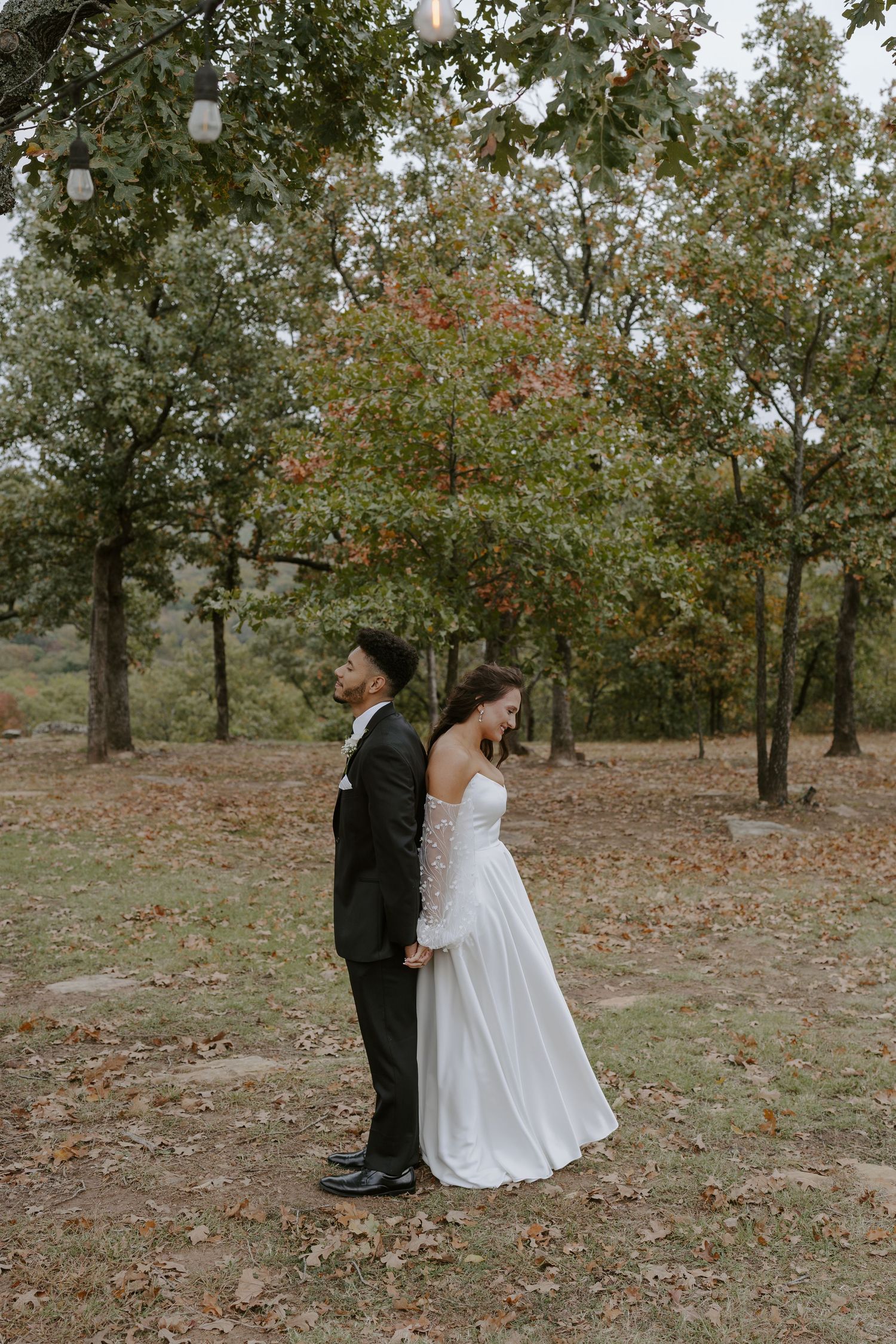 A bride and groom embrace in a scenic fall setting with scattered leaves on the ground.