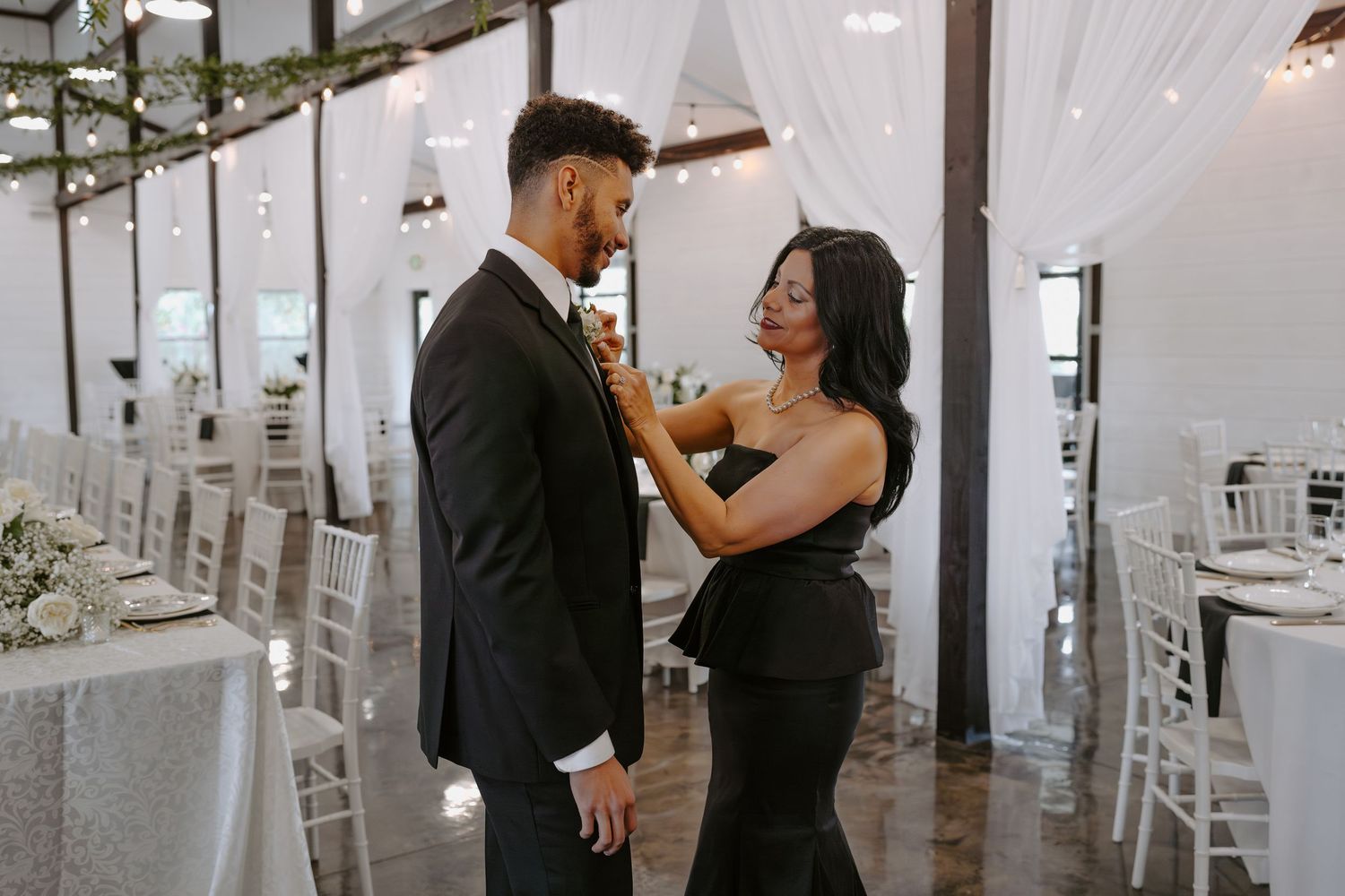 A couple embraces in an elegant white-draped venue with polished floors and modern decor.