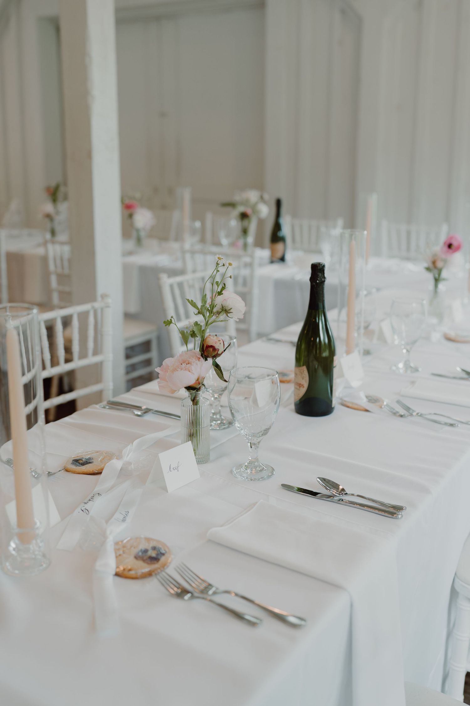 Elegant white wedding reception table setting with wine glasses and delicate floral centerpieces.