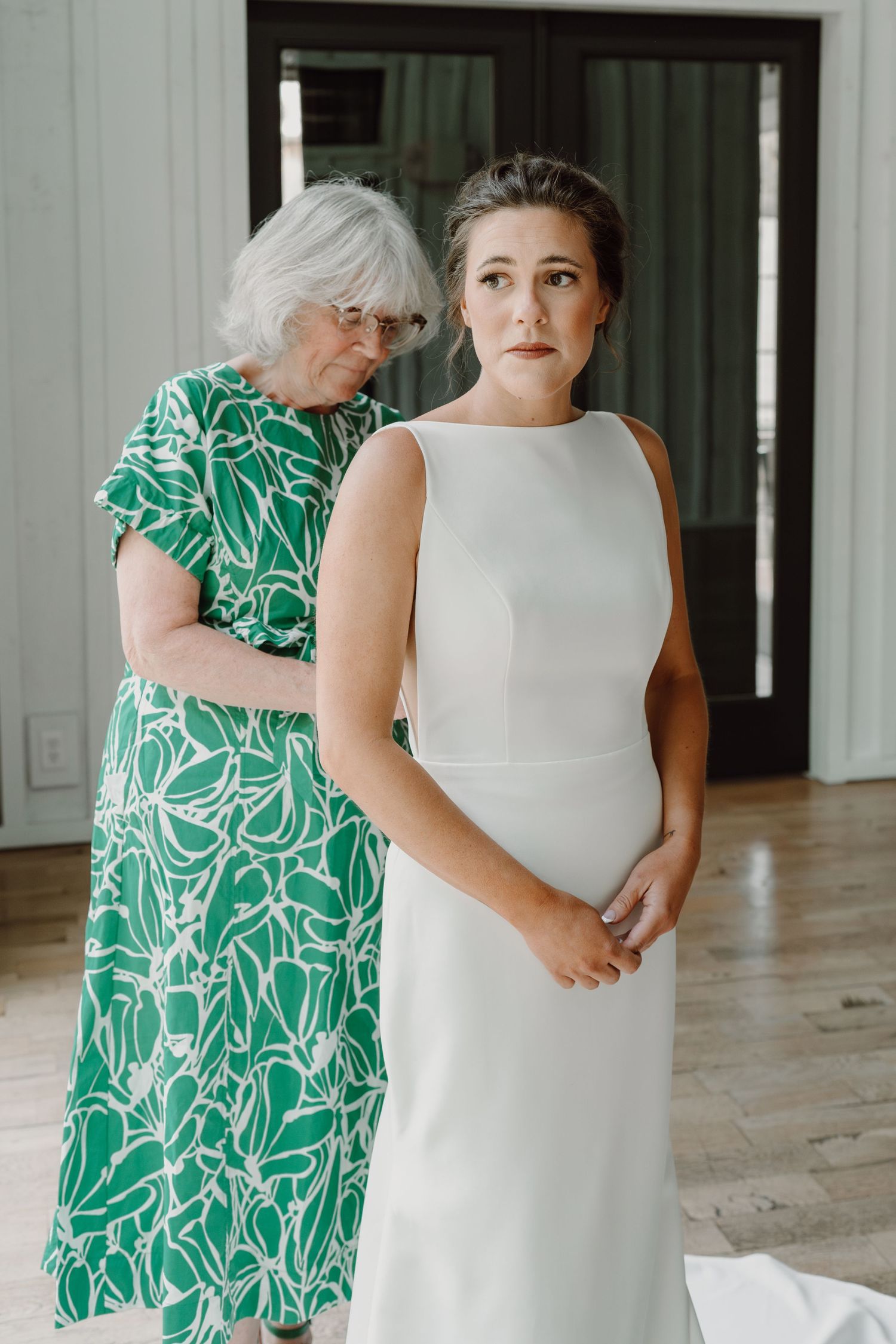 A touching moment between a bride in a sleek white dress and someone wearing a vibrant green patterned dress.