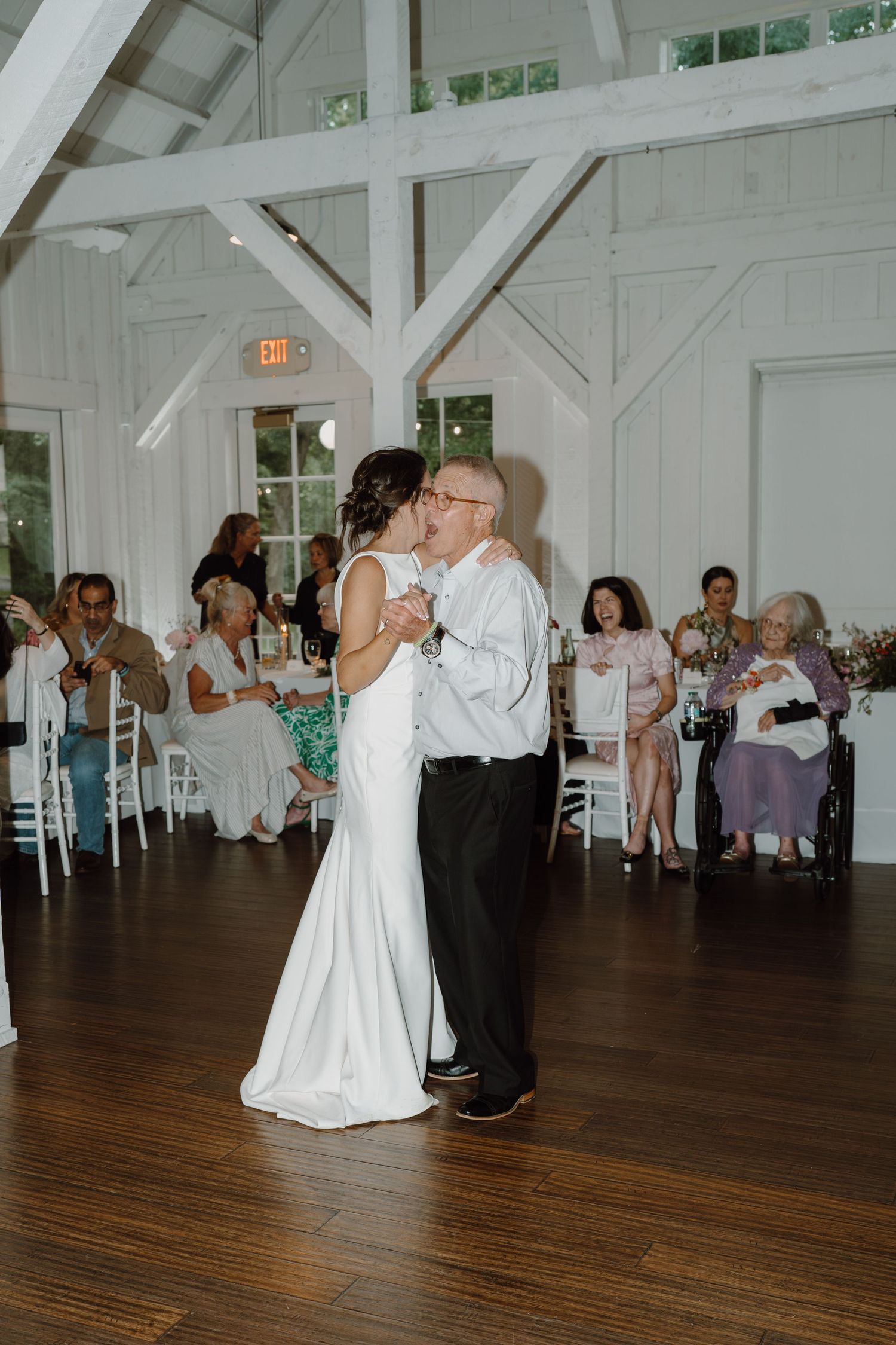 Intimate dance moment captured in a rustic white barn reception space surrounded by seated guests.