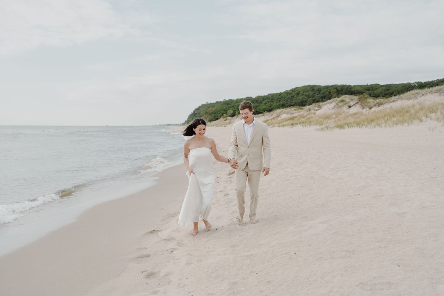 Couple in light colored clothing walking together on a scenic coastal beach.
