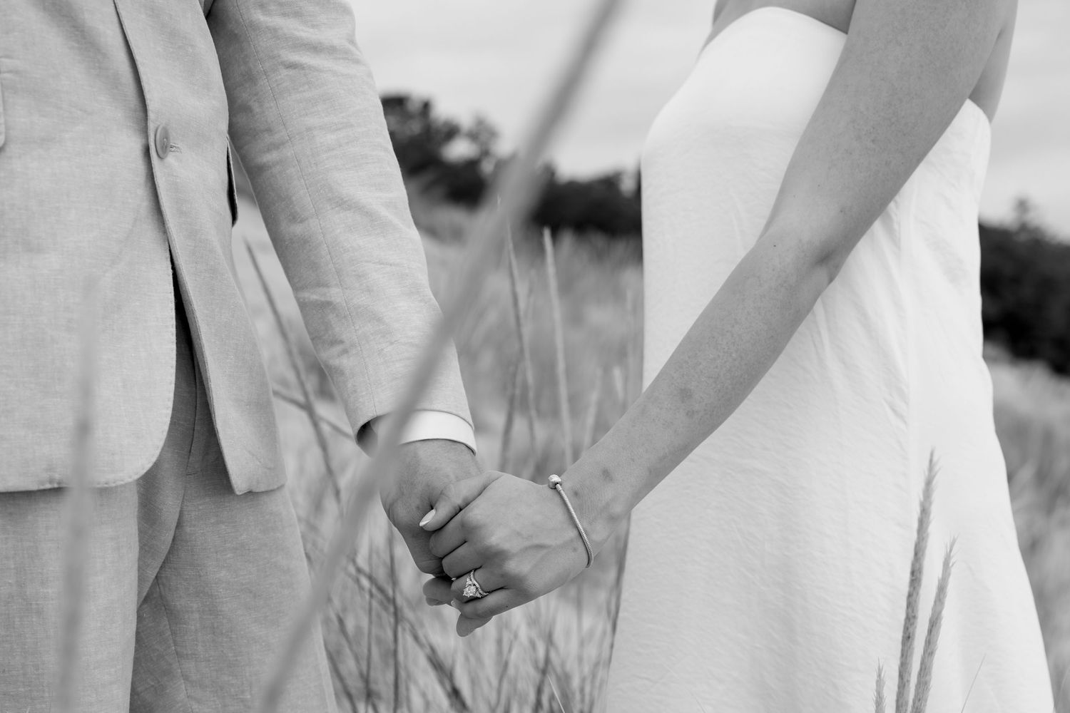 Black and white photo showing a couple in formal attire standing among beach grass.