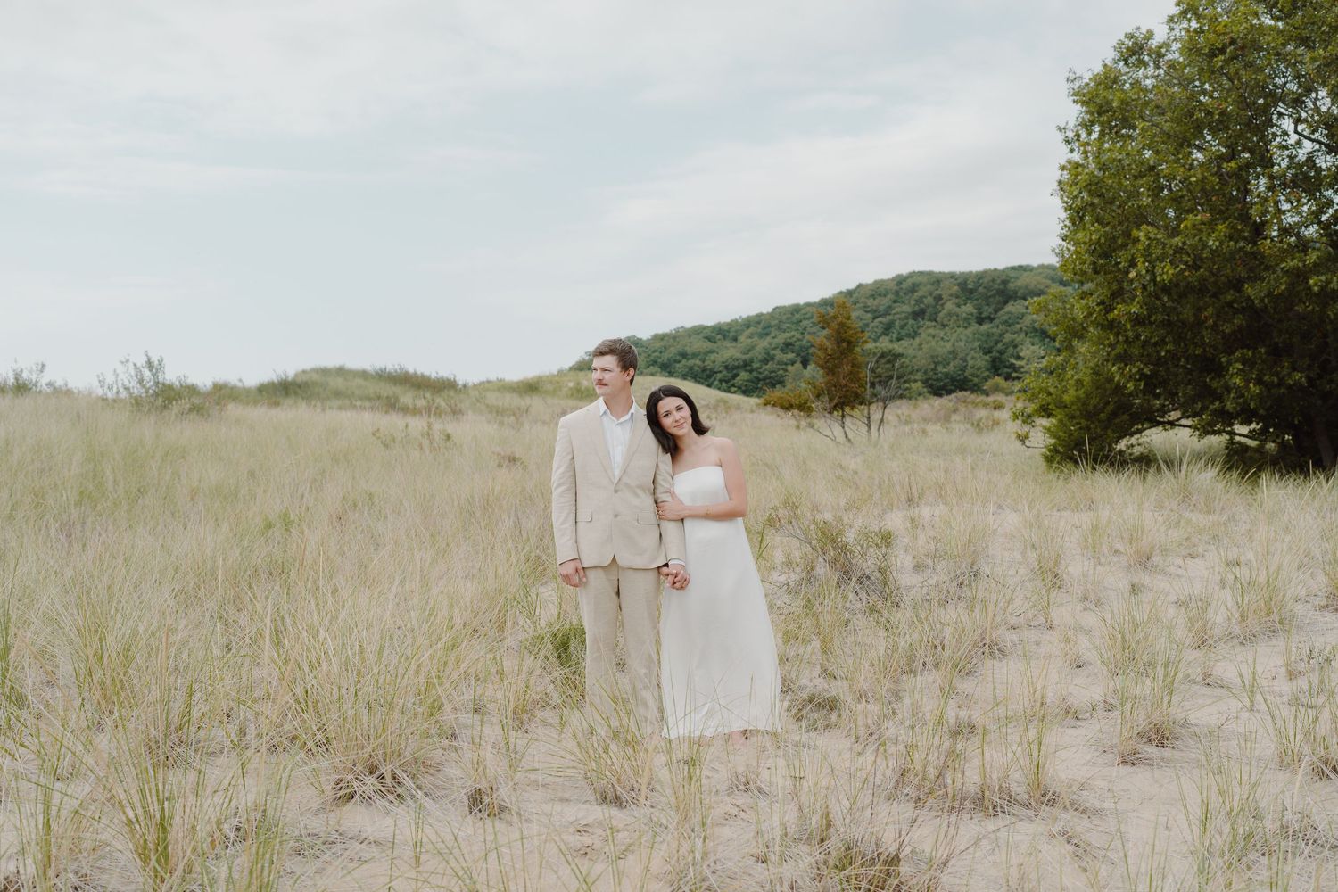 A romantic wedding photo of a couple standing among coastal dune grass.