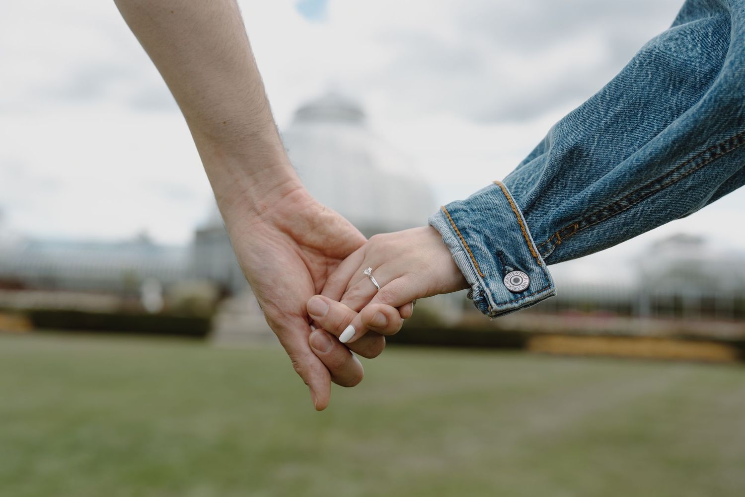 Two hands reaching towards each other in front of a glass conservatory building.
