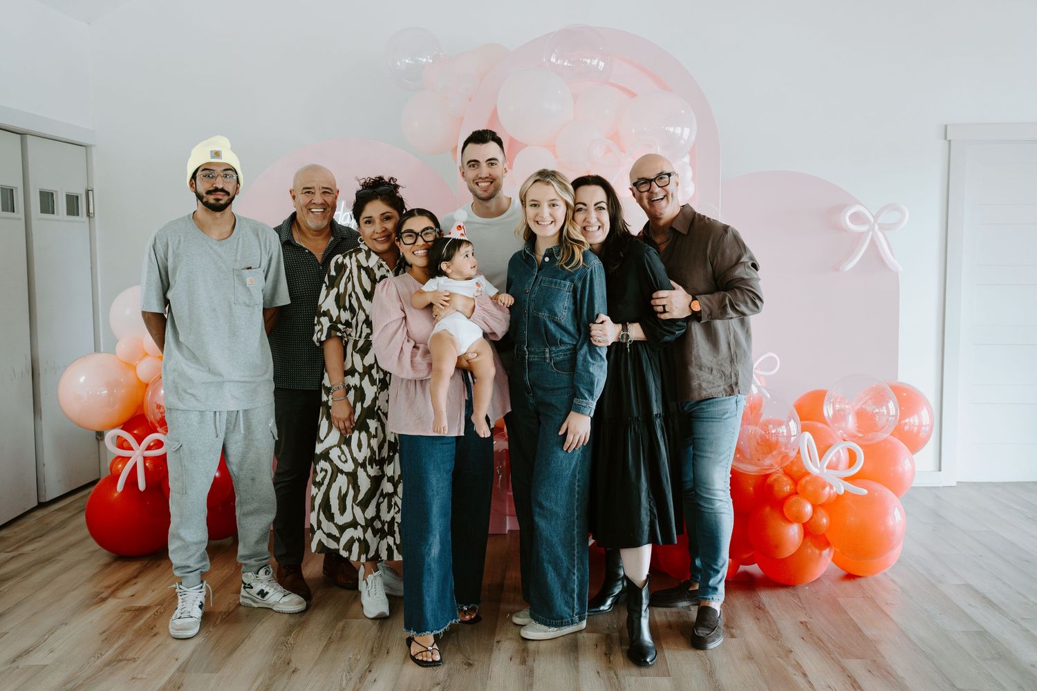 A family gathering poses together against a festive balloon display with pink and orange colors.