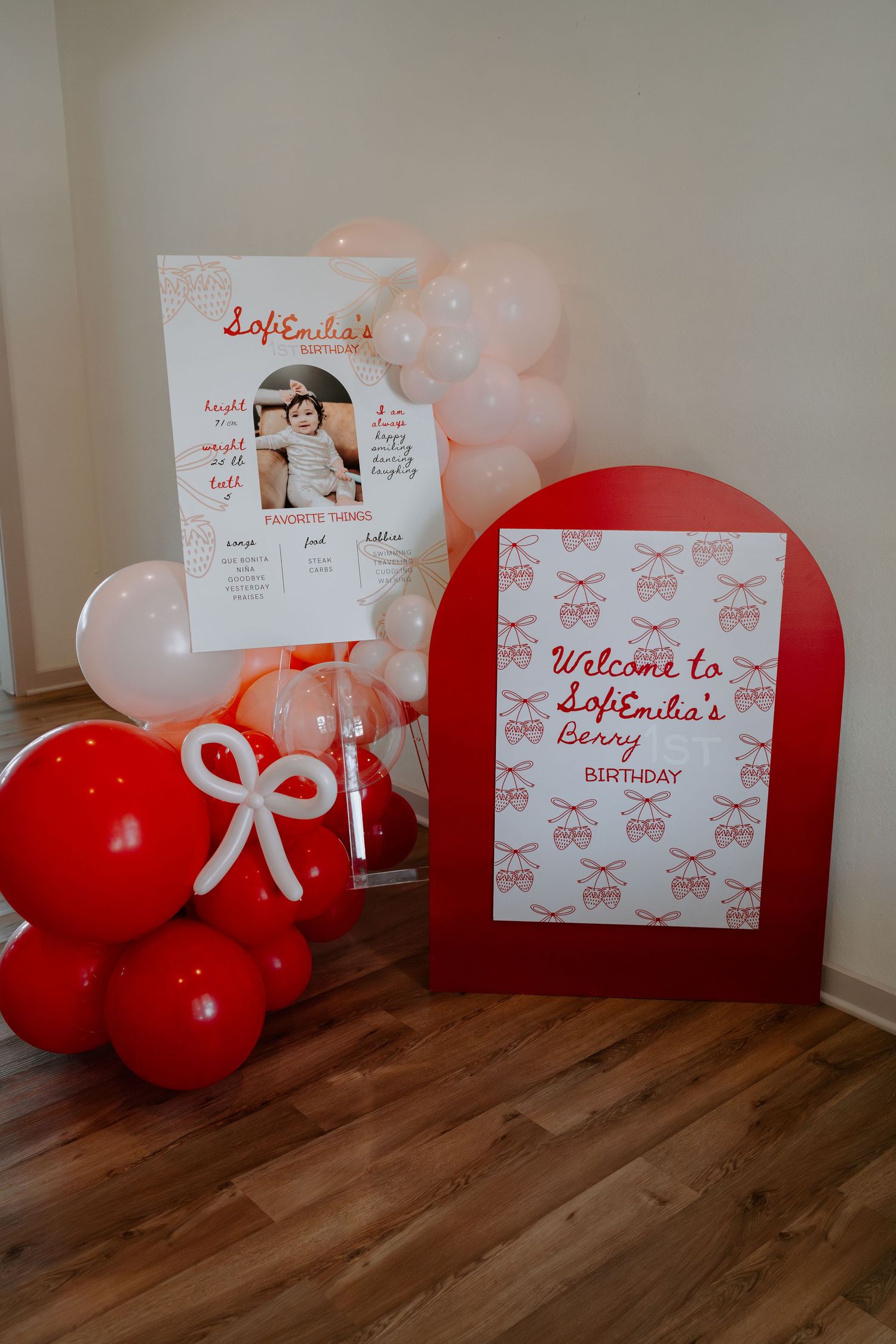 Red and white balloon decorations with welcome signs arranged on hardwood floor.