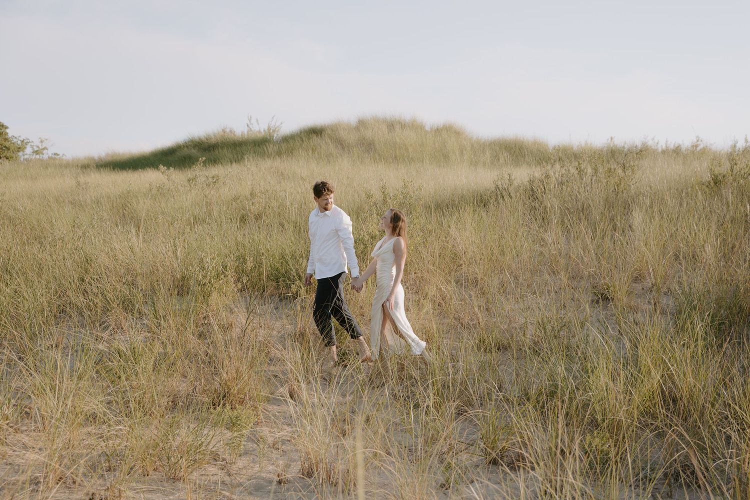 Two figures walk together across a scenic hillside covered in tall grass.