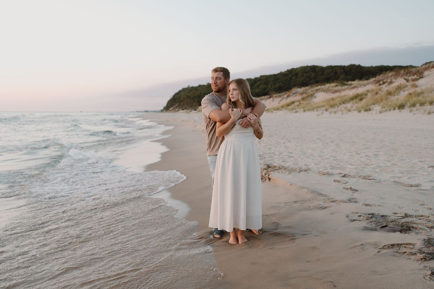 Couple walking along a scenic beach shoreline at sunset with waves gently rolling in.