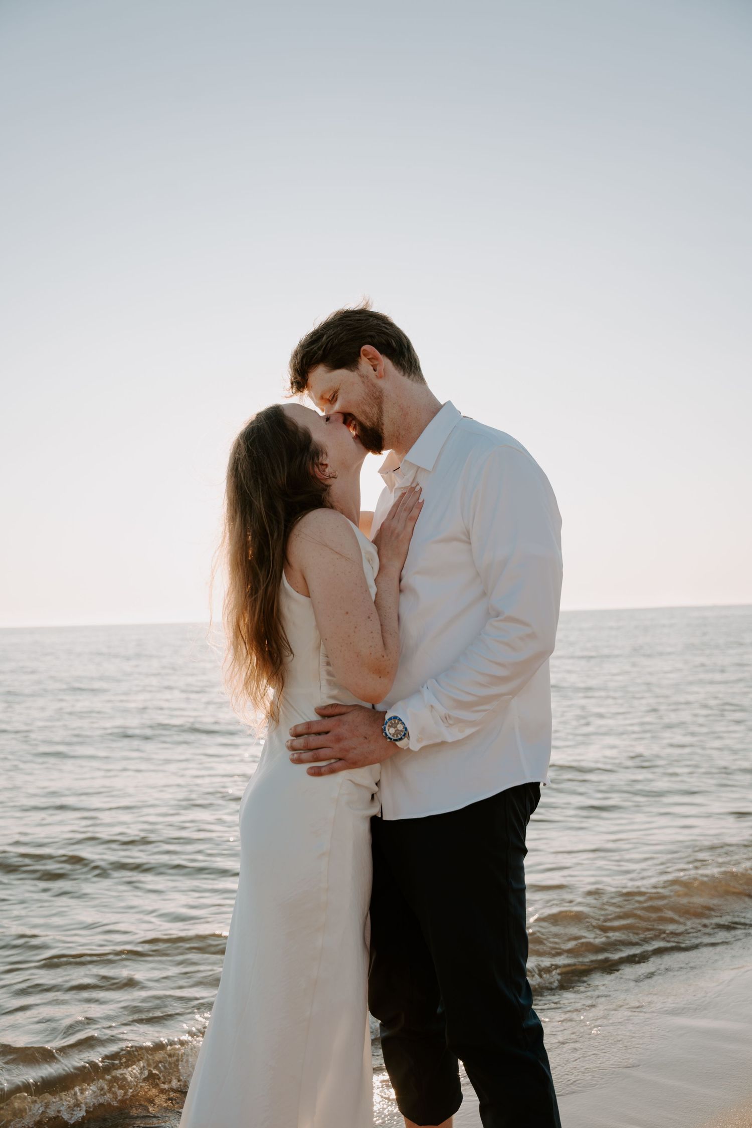 Intimate moment between couple in formal attire on sandy beach during golden hour.