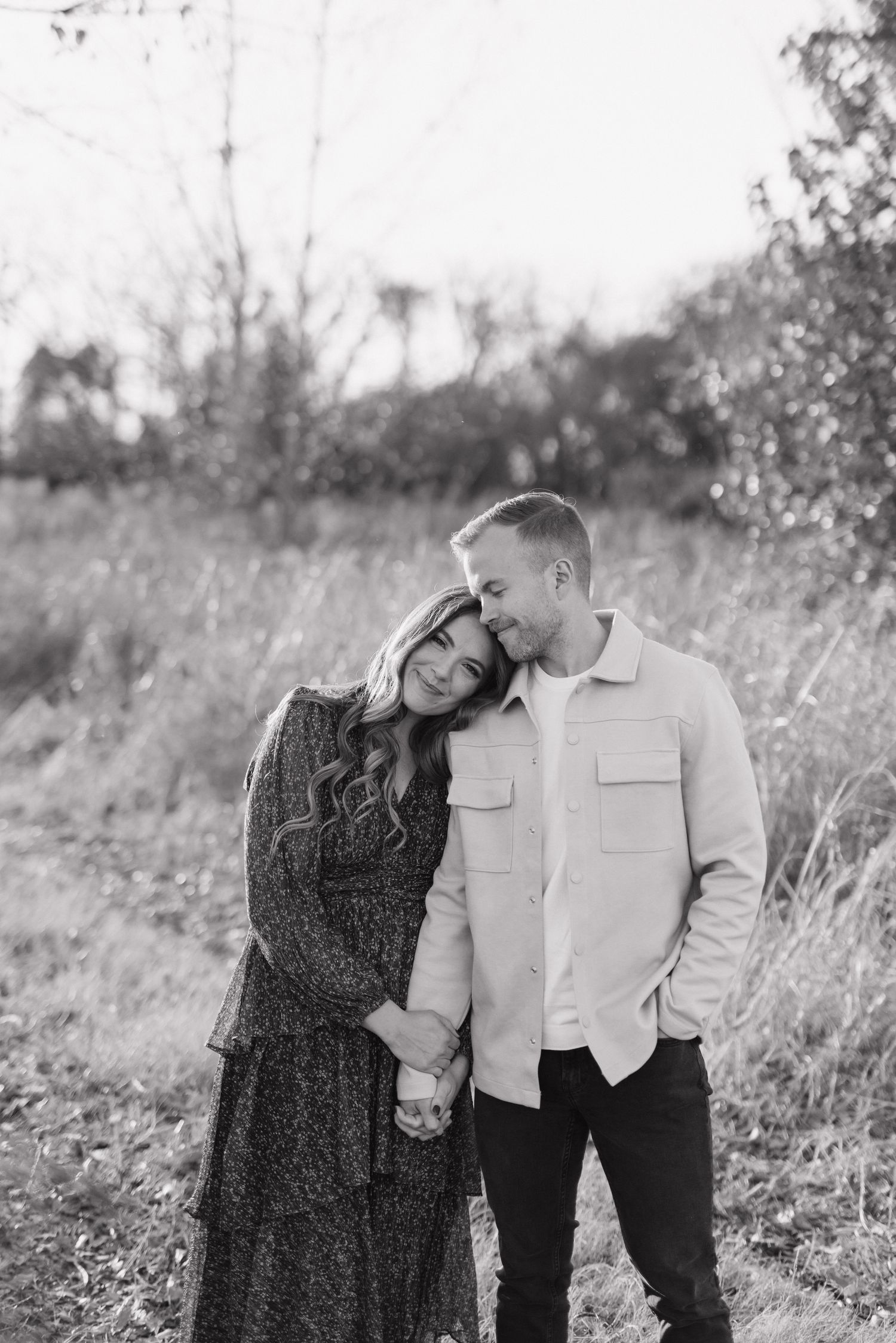 A romantic couple embraces in a field during a black and white photoshoot.