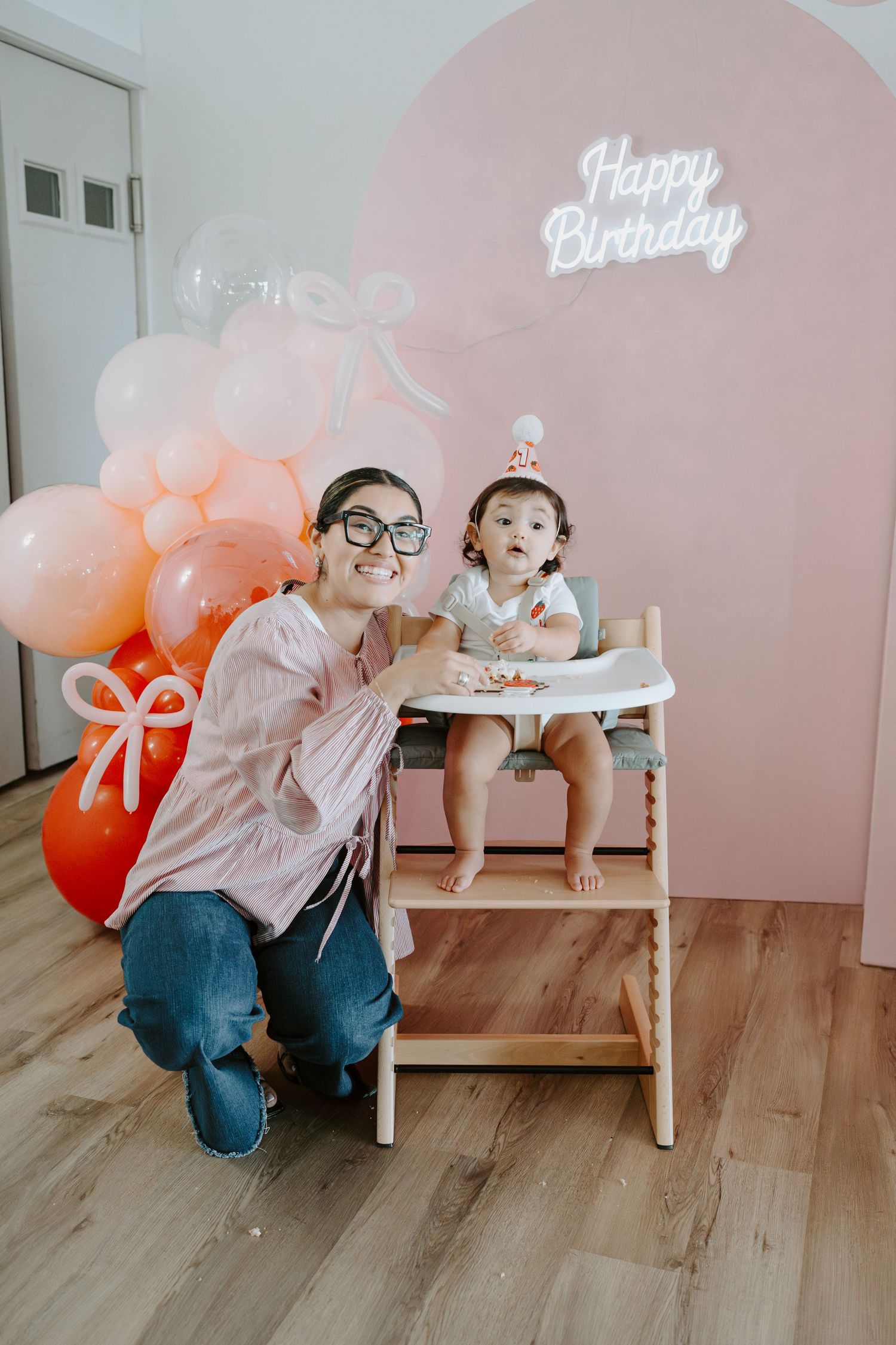 Birthday celebration setup with pink balloons and neon signage in a minimalist room.