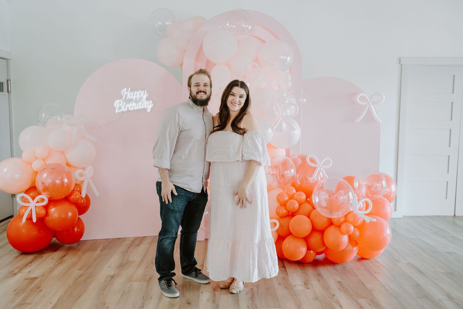 A family photoshoot setup with pink and orange balloon decorations against a white wall.