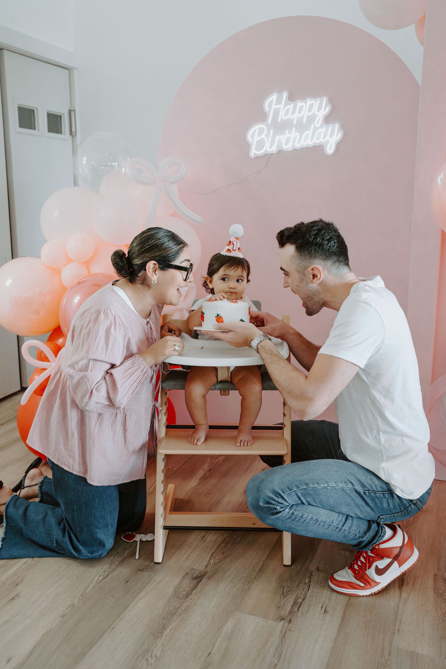Family gathered for birthday celebration with decorative pink backdrop and wooden table setup.