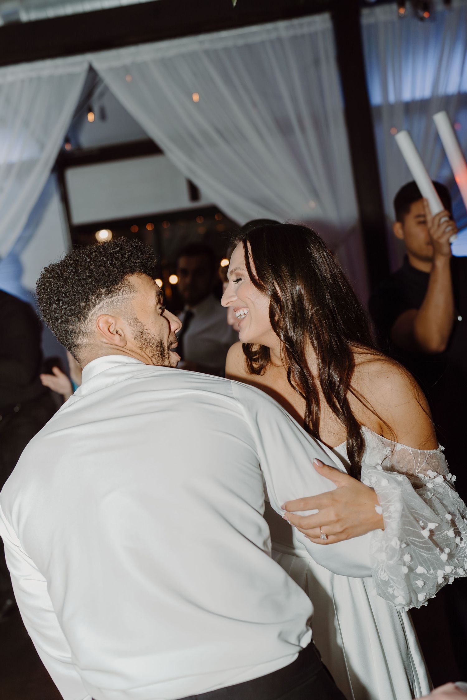 A couple shares an intimate dance moment under white draped fabric and soft lighting.