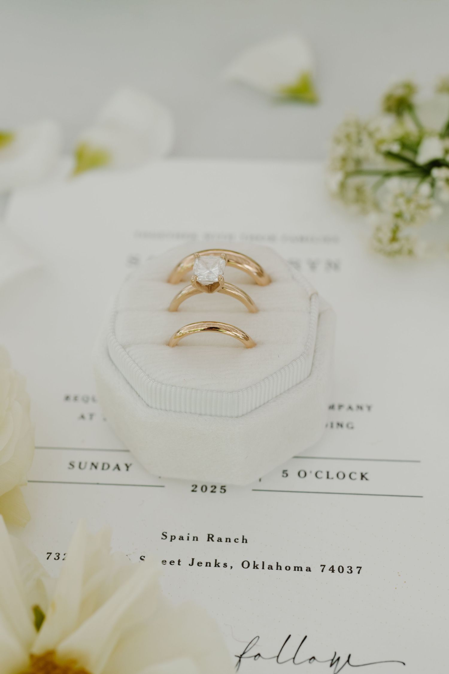 Wedding invitation and gold rings styled with floral elements on white surface.