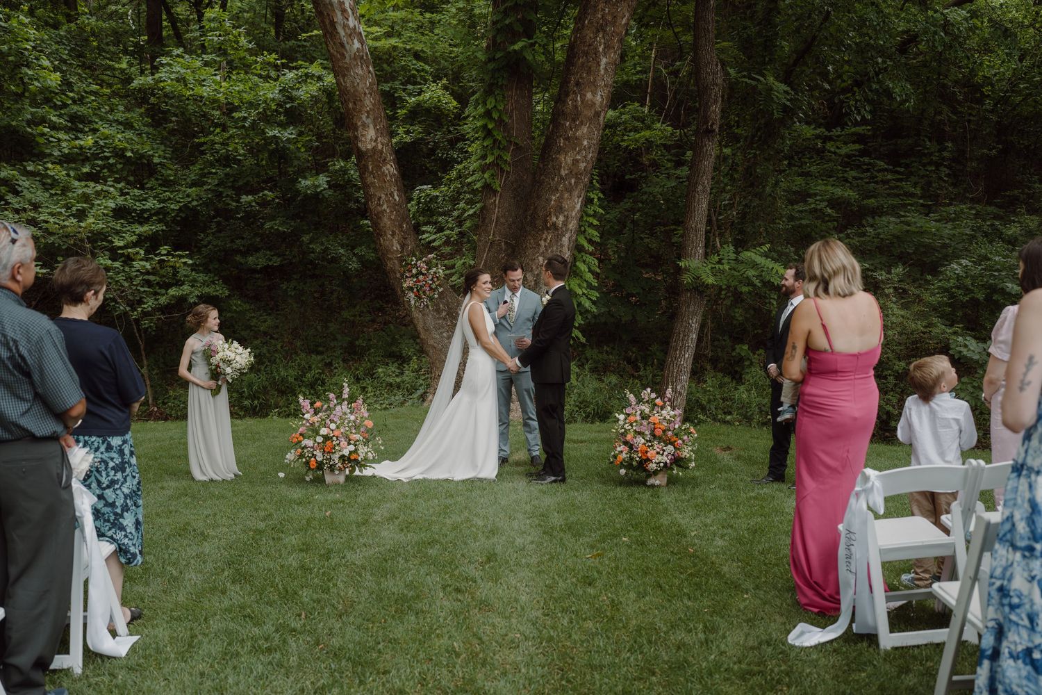 Wedding guests gather for photos in a wooded outdoor setting during the ceremony.