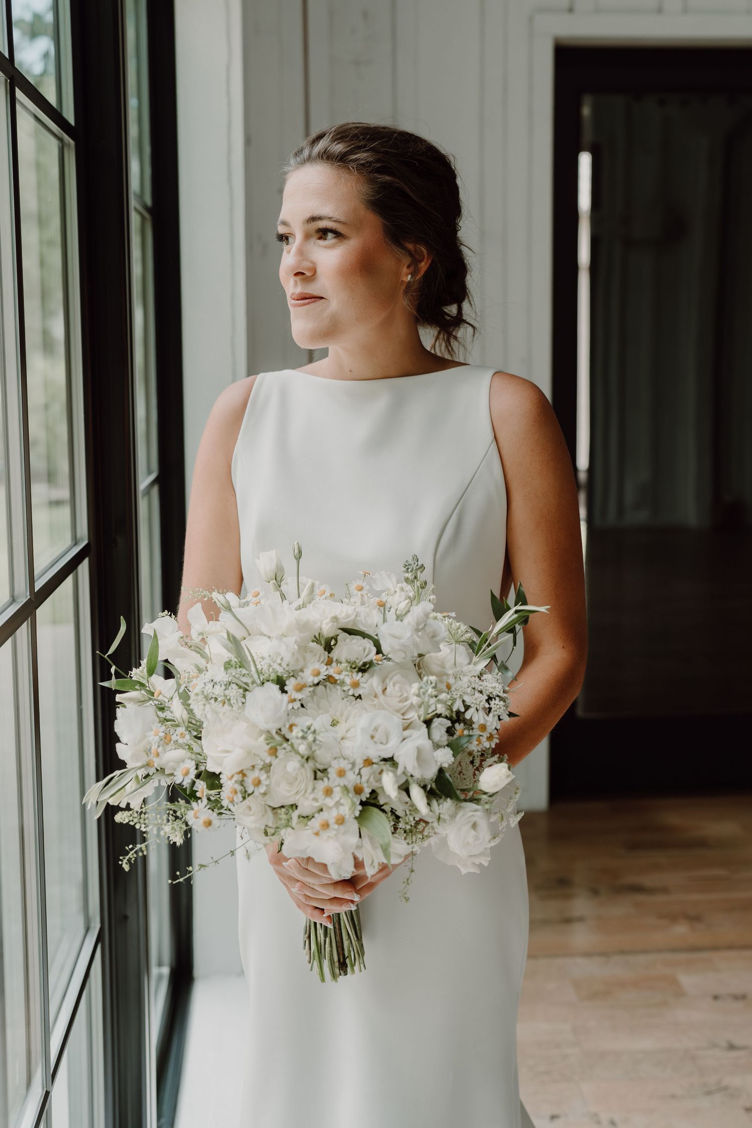 Bride in sleek white dress holding an elegant white floral bouquet.