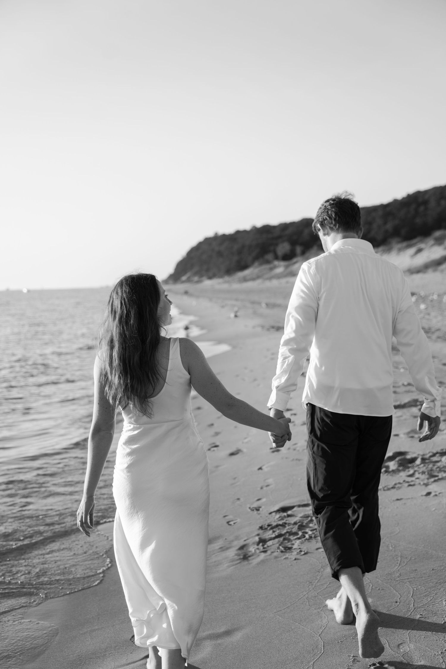 Black and white image of a couple walking barefoot along the water's edge.