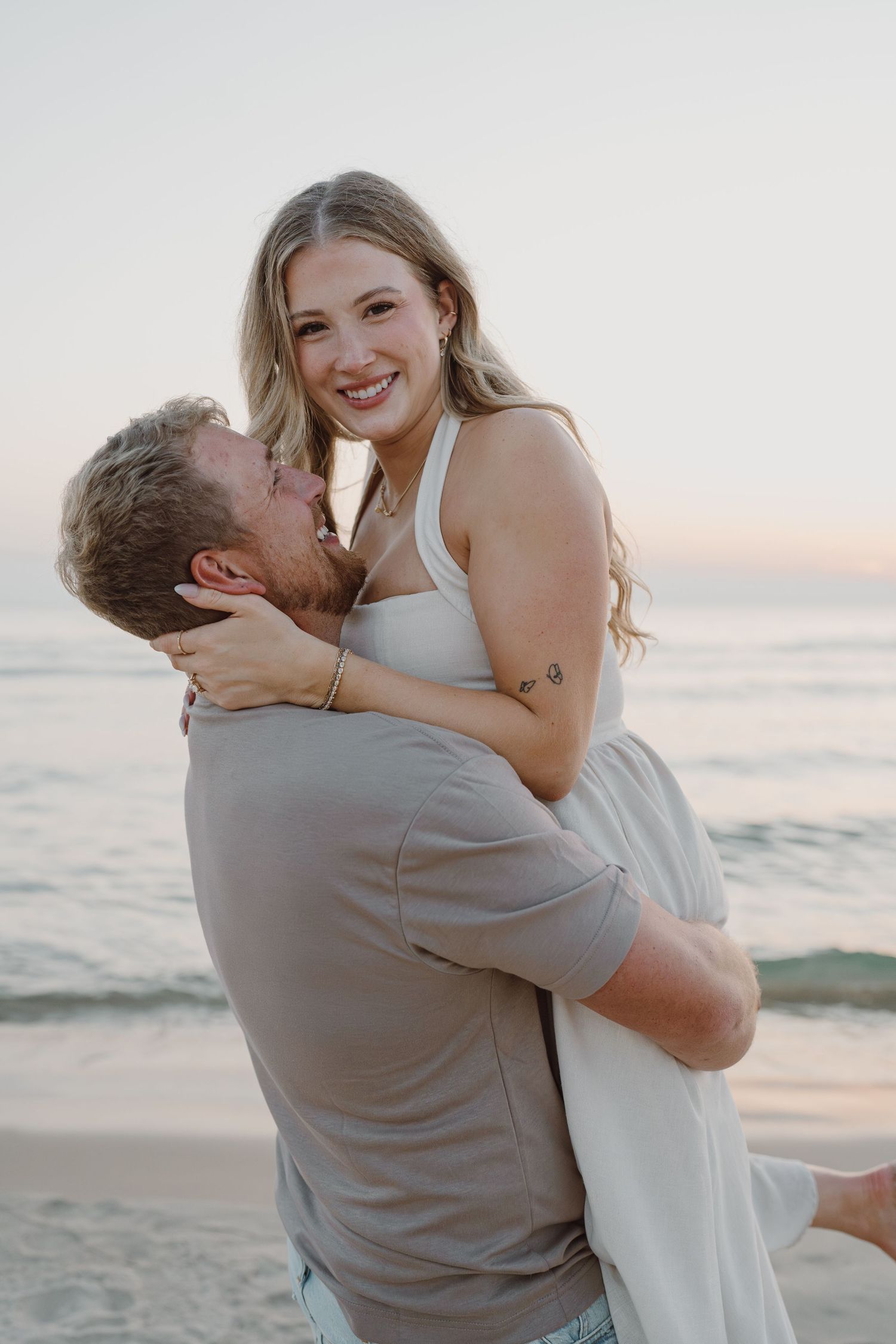 A joyful couple shares laughter and embraces during their sunset beach photoshoot.