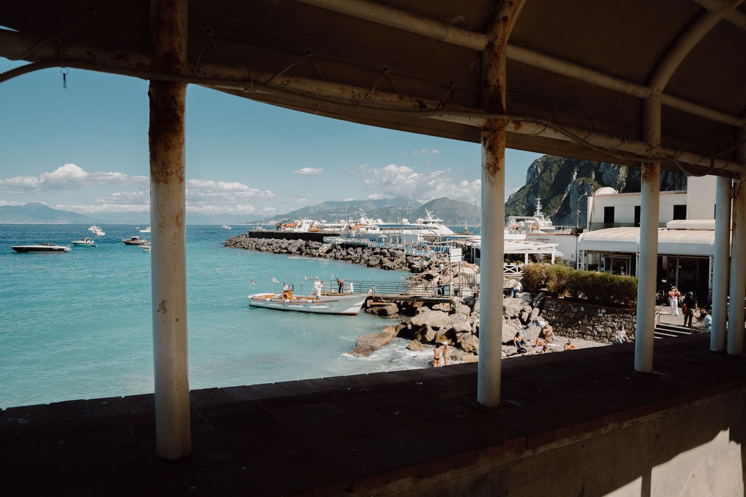 Panoramic ocean view through a covered terrace showing boats and coastline.