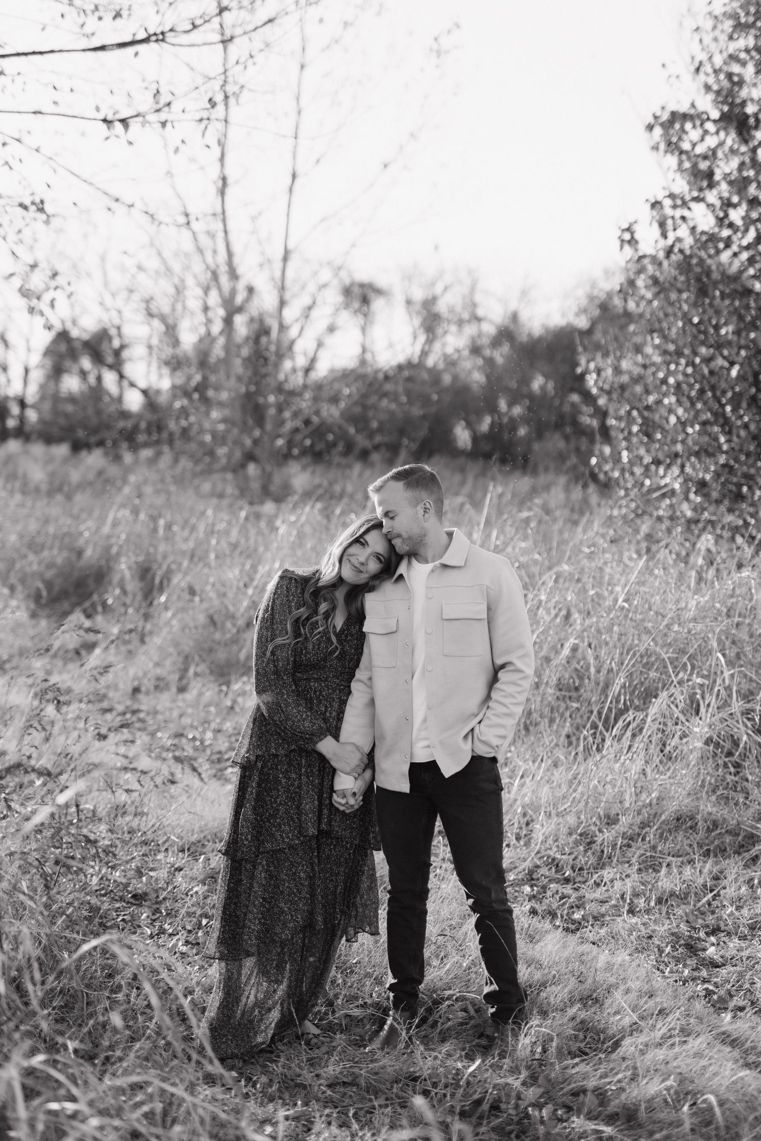 A couple poses together in a misty field with tall grass in black and white.
