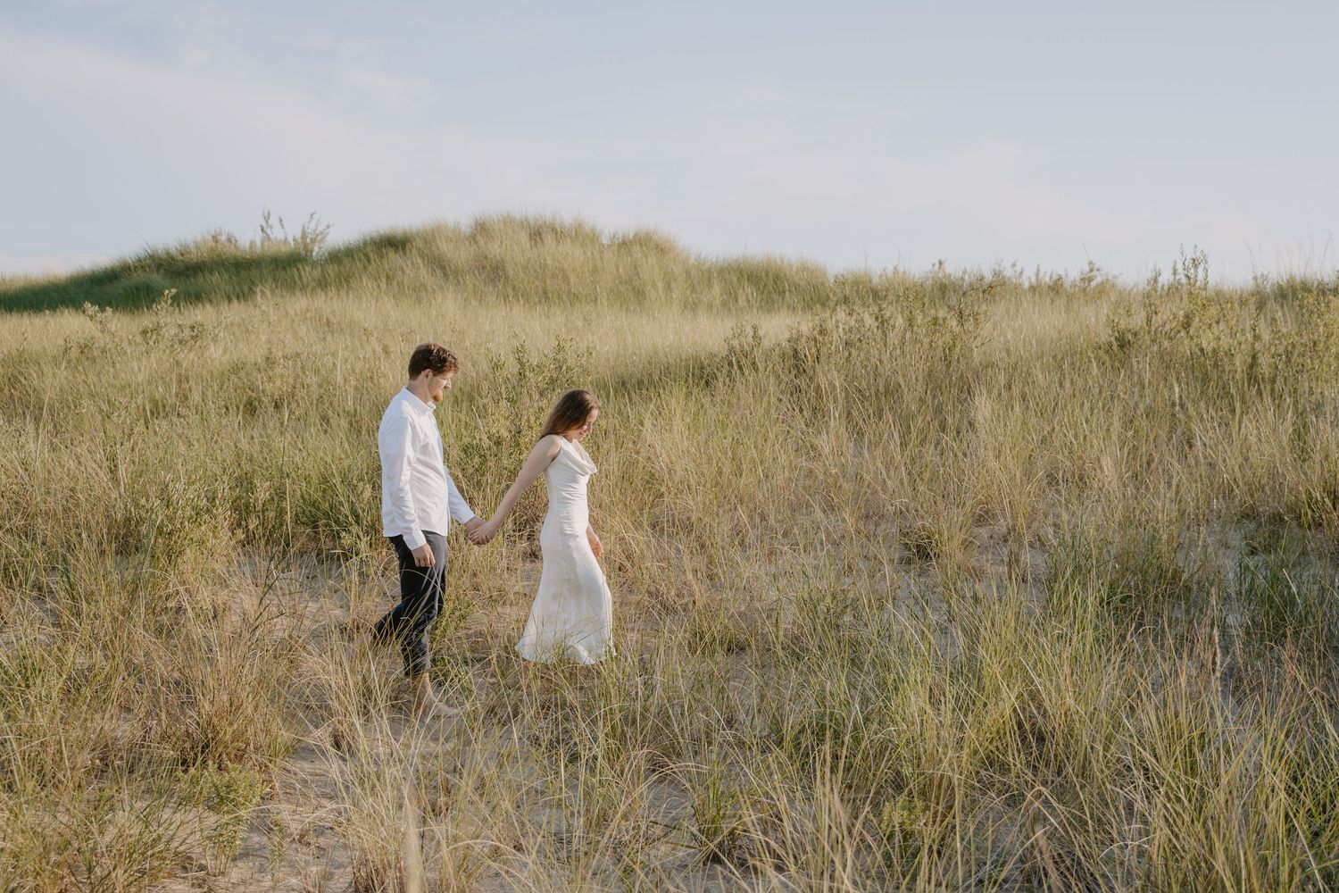 Two people walk together through a golden field of tall grass on a sunny afternoon.