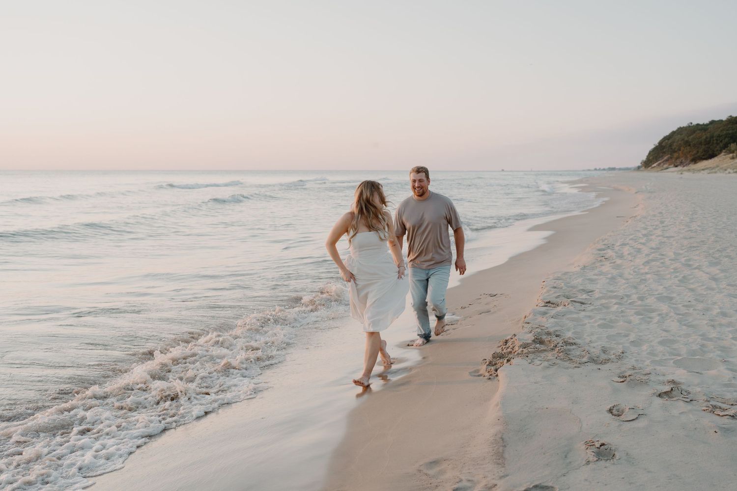 A couple walks along a serene beach at sunset holding hands with ocean waves in the background.