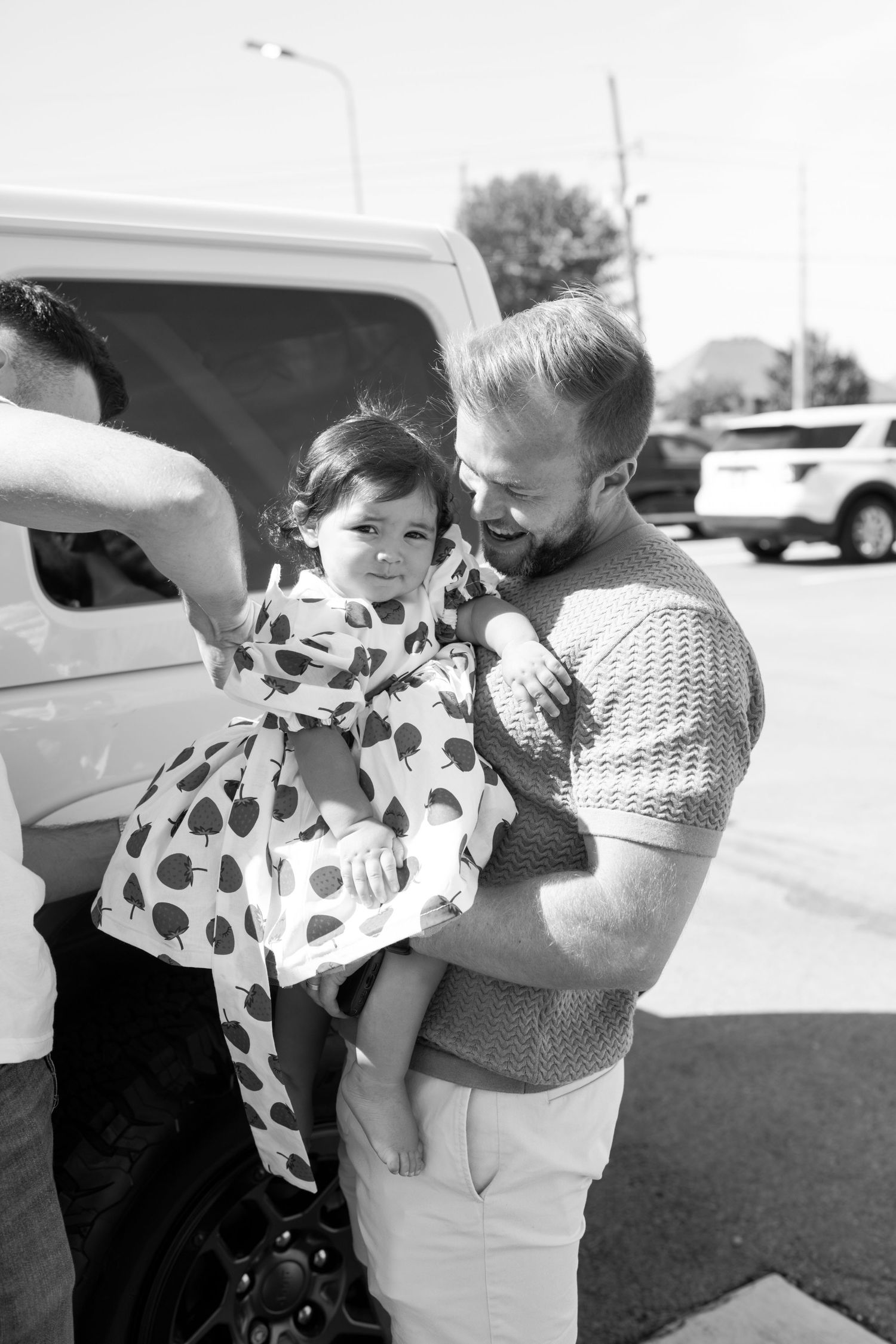 Black and white photo of people interacting in a parking lot.